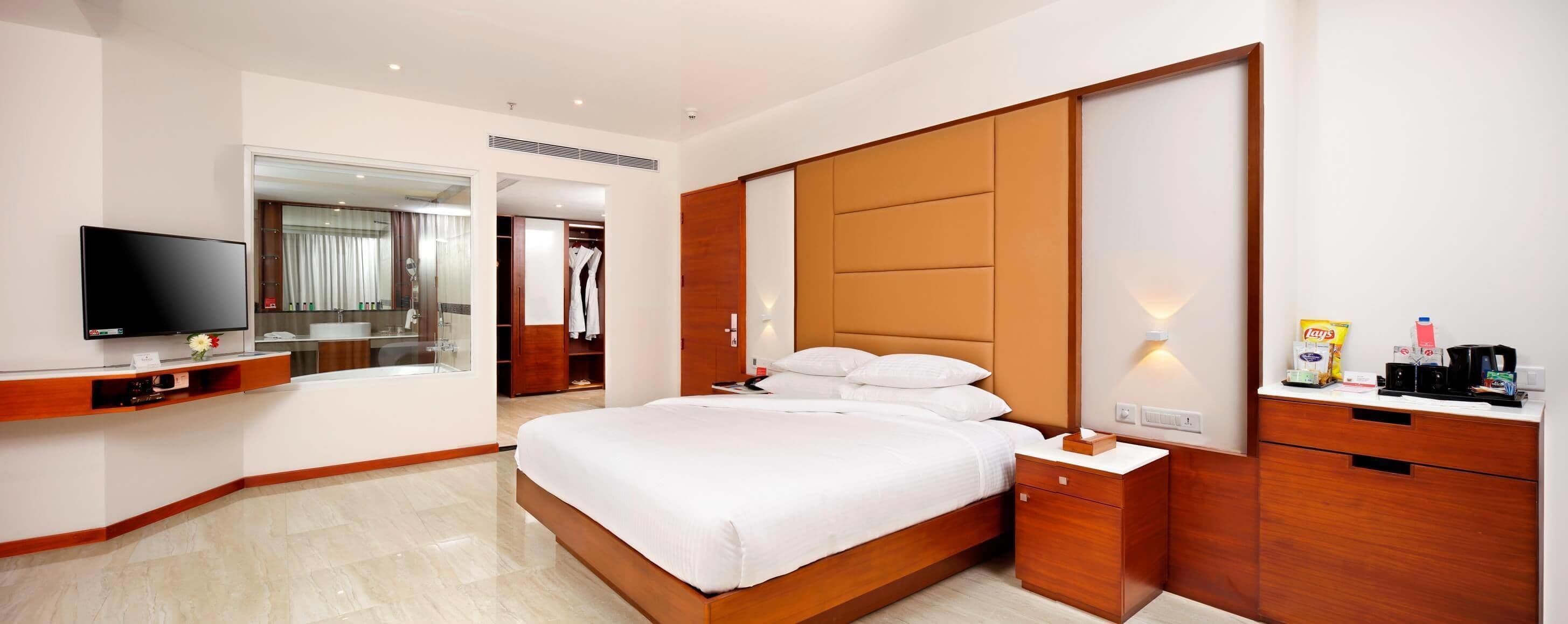 Ein Hotelzimmer mit Bett, Fernseher, Schreibtisch, Kleiderschrank und einem Badezimmer, das durch eine offene Tür sichtbar ist.