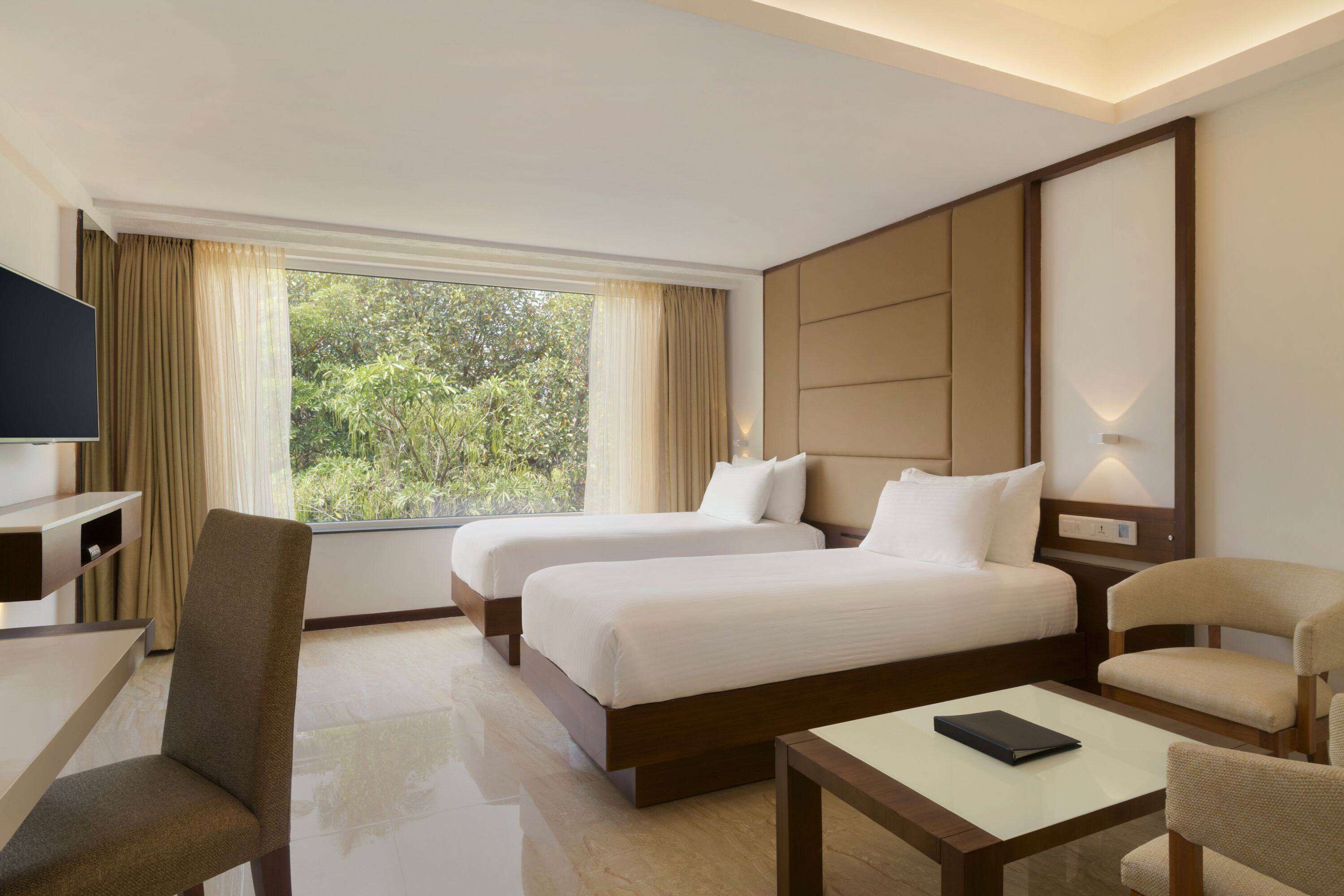 A hotel room with two beds, a TV, a desk, and a chair.
