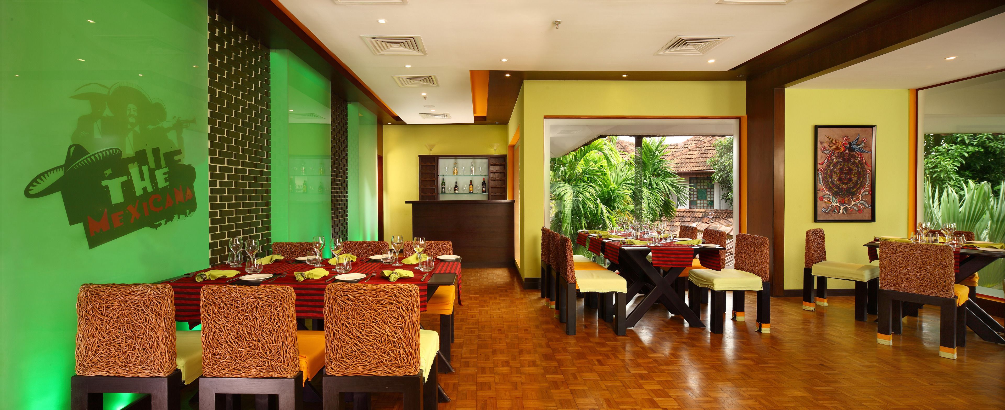Un restaurante con pared verde, sillas de mimbre y suelo de madera.