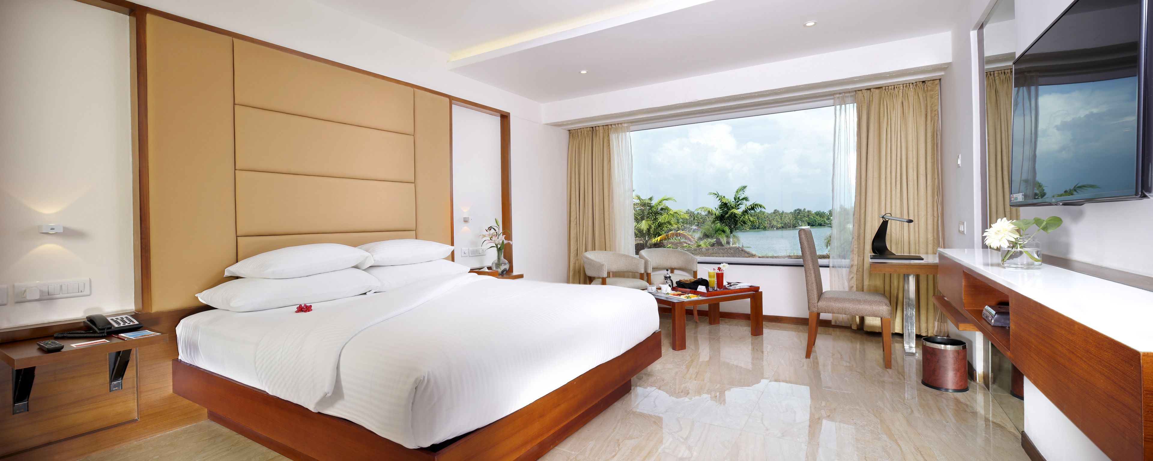 A hotel room with a large bed, a desk, a chair, a small table, and a view of the outdoors.
