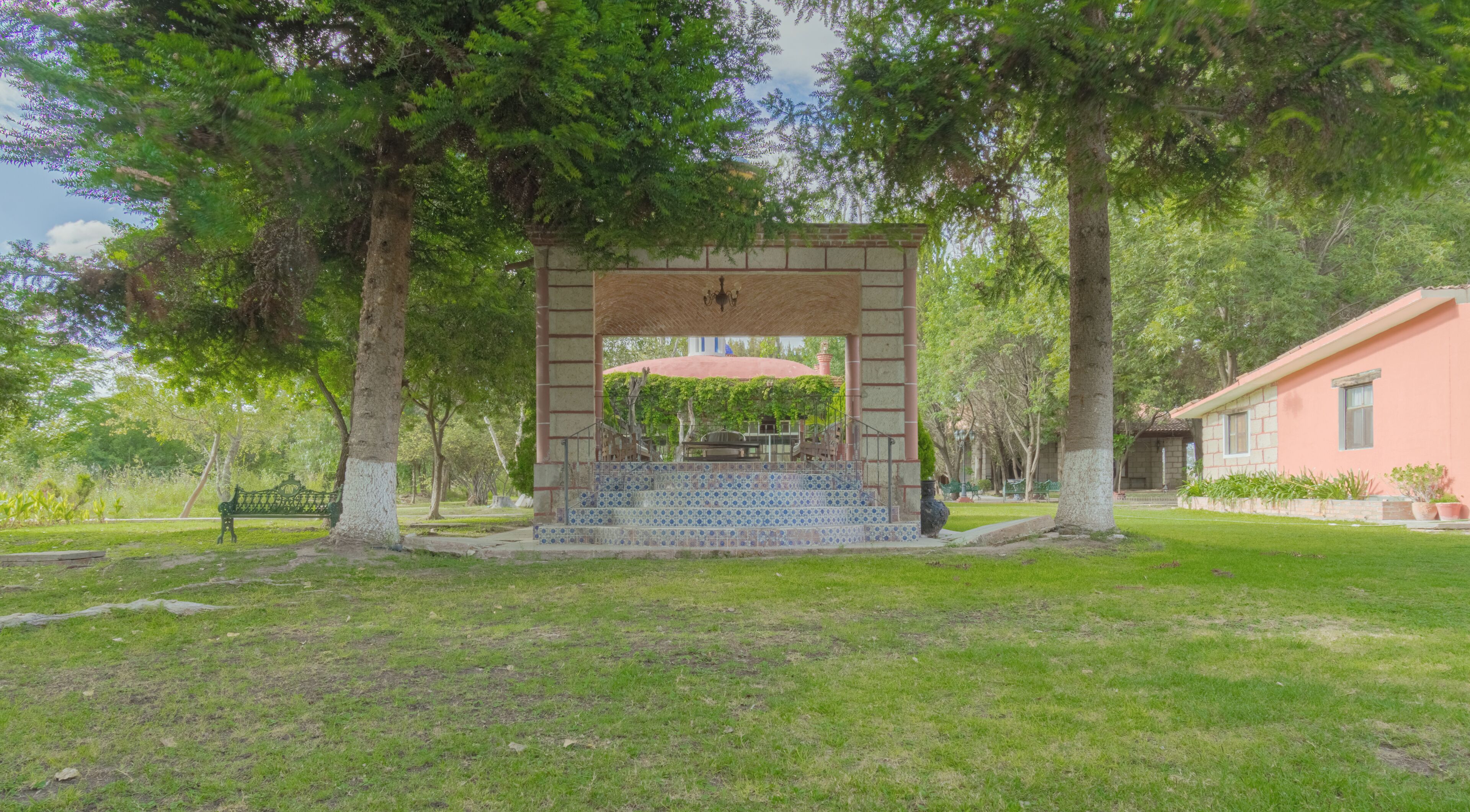 A gazebo with a tiled floor and a red roof, surrounded by trees and grass.