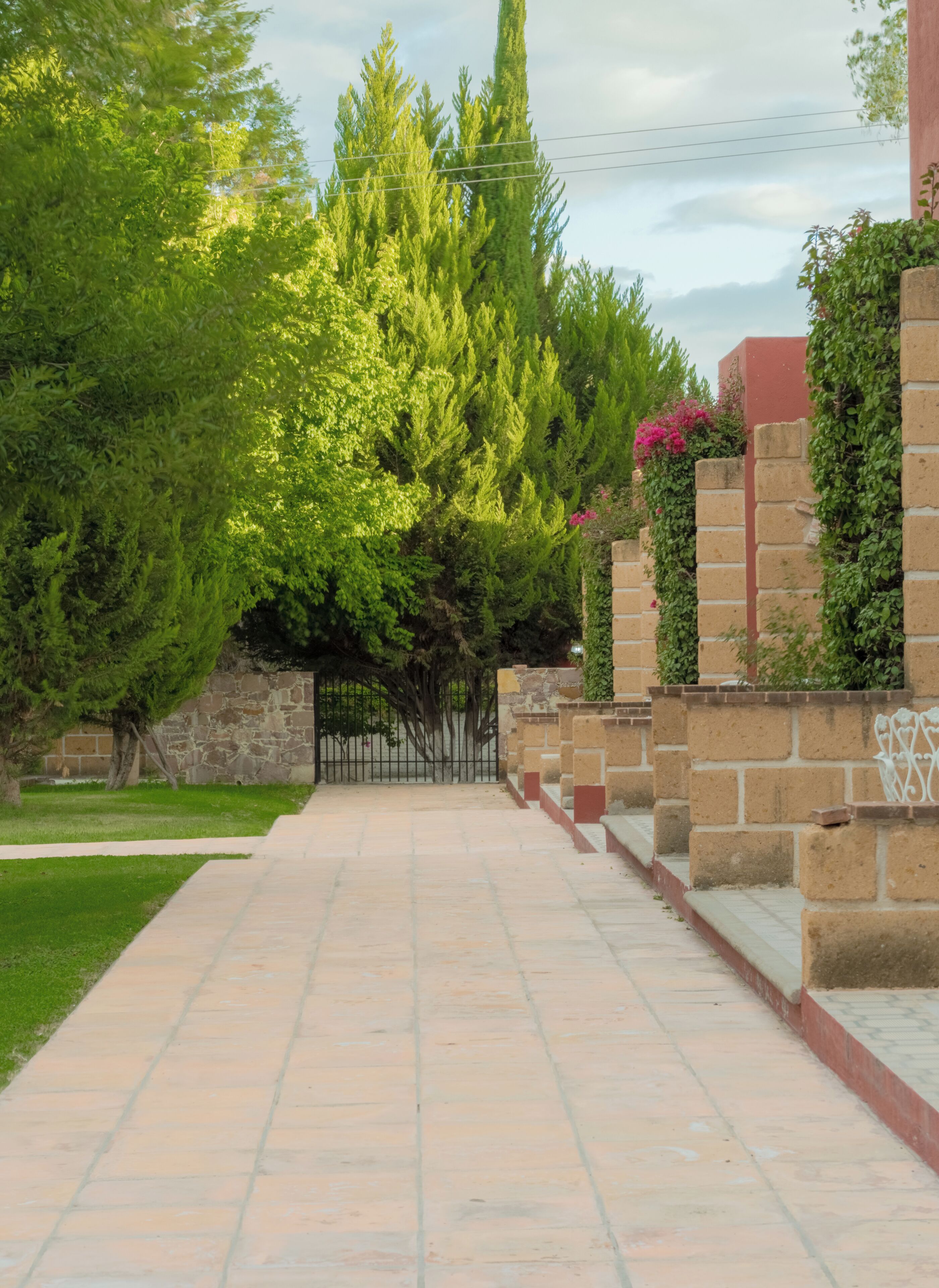A paved pathway leading to a building with stone walls and greenery.