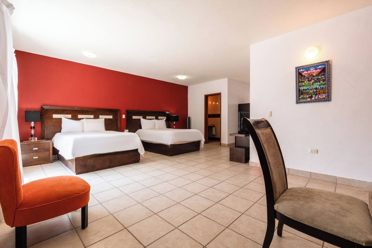 A hotel room with two beds, a chair, a desk, and a wall-mounted TV.