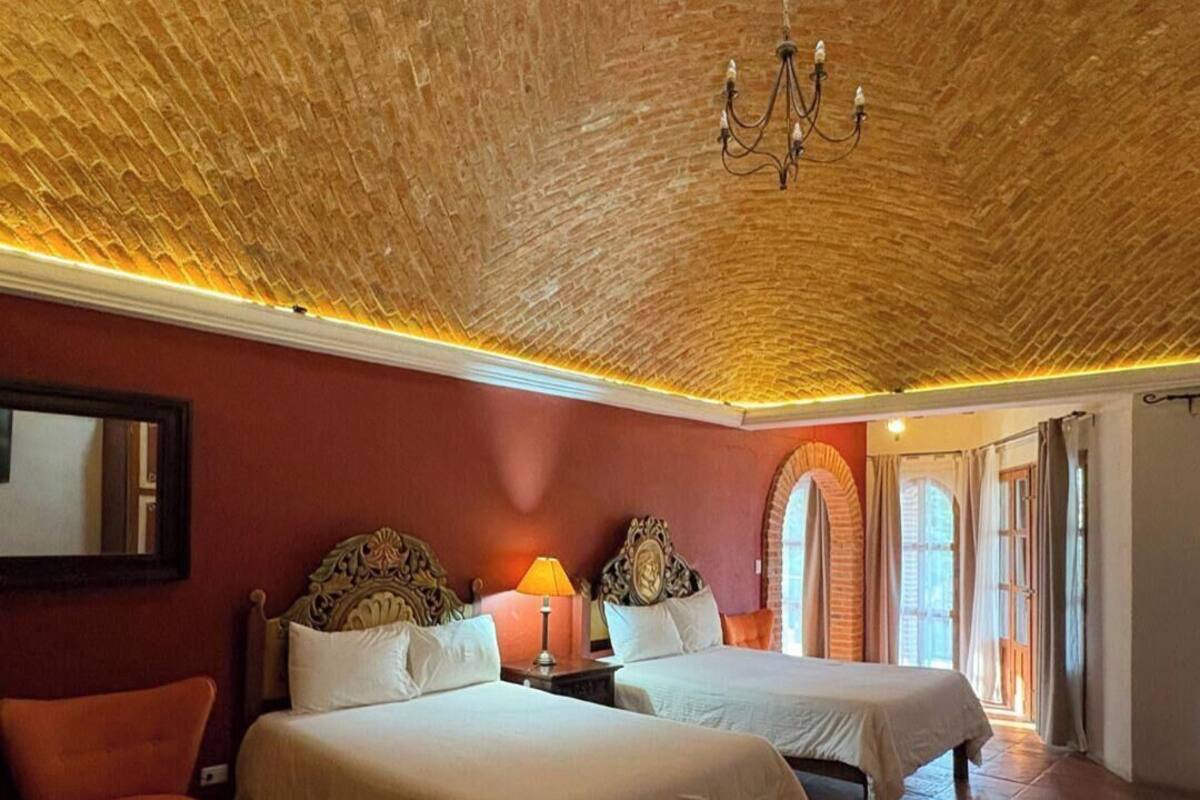 A hotel room with two beds, a chandelier, a large skylight, and a red wall.