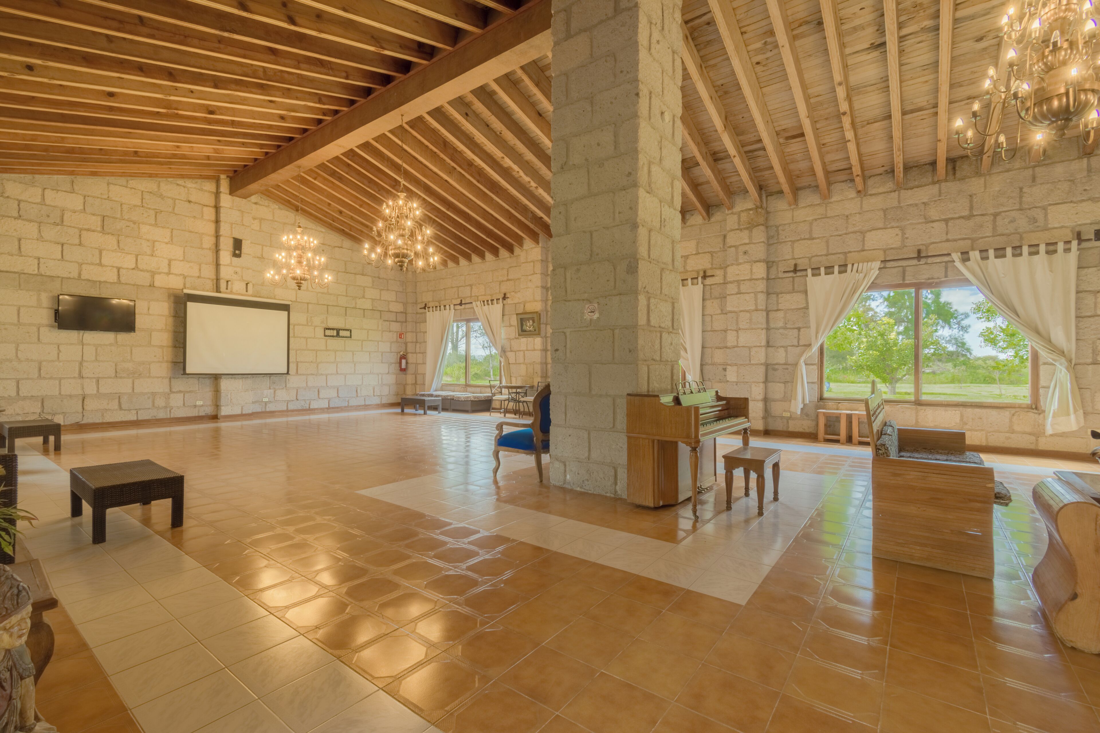Un grand hall doté d’un haut plafond, de poutres en bois, d’un piano et d’un écran de projection.
