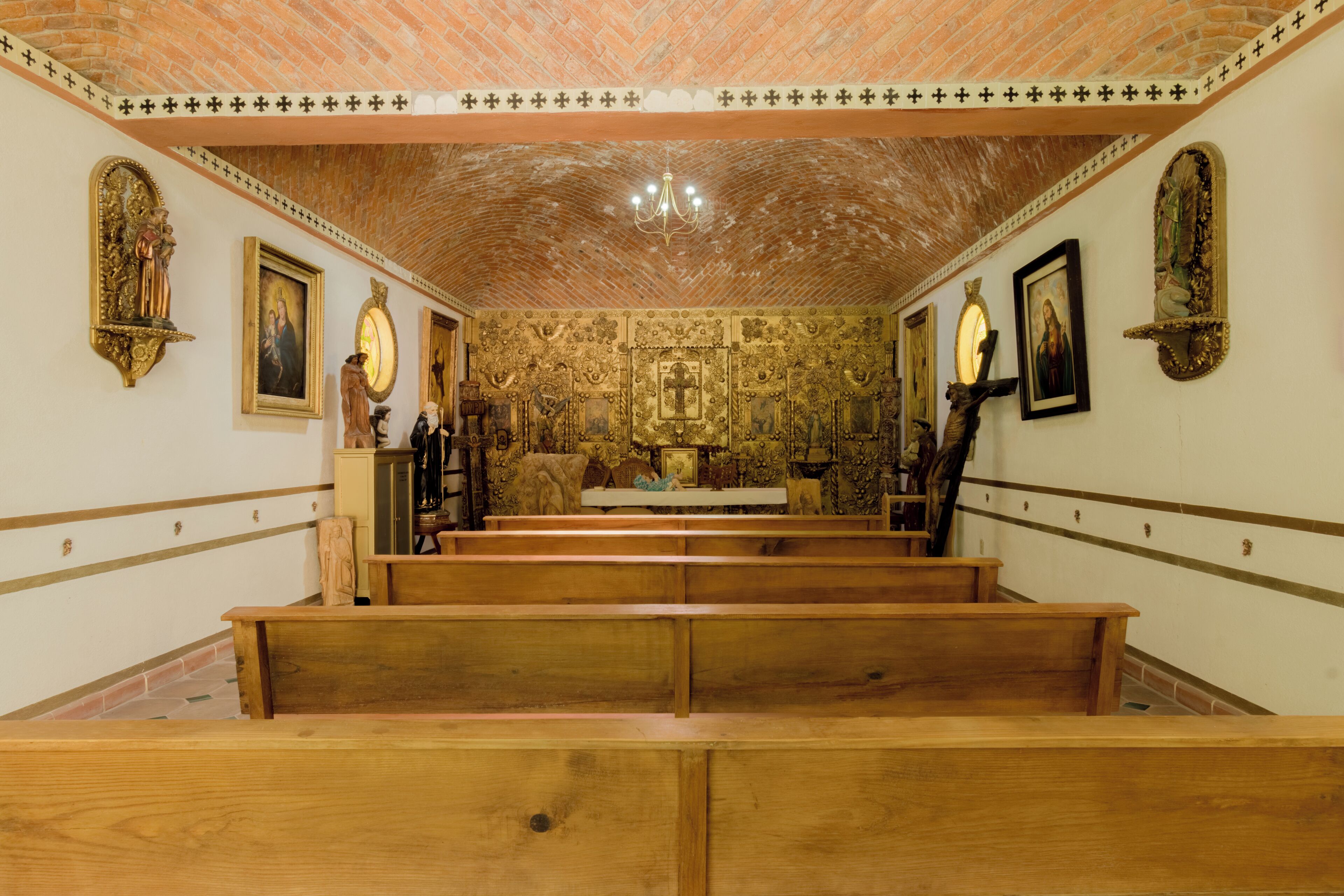 Interior de iglesia con bancales de madera, pinturas religiosas y techo de ladrillo.