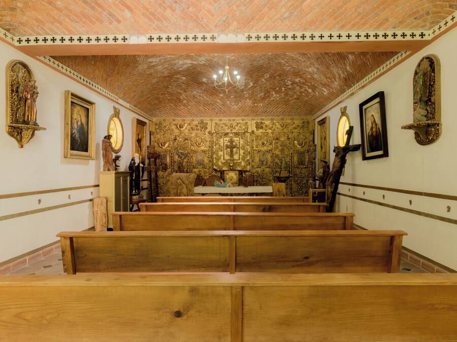 Interior de iglesia con bancales de madera, pinturas religiosas y techo de ladrillo.