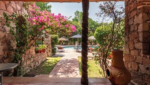 A patio area with a stone wall, a wooden table, a large vase, and a view of a pool and garden. - Hotel Atotonilco El Viejo (San Miguel de Allende)