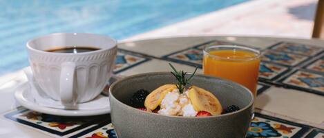A table with a bowl of breakfast, a cup of coffee, and a glass of orange juice by a pool.