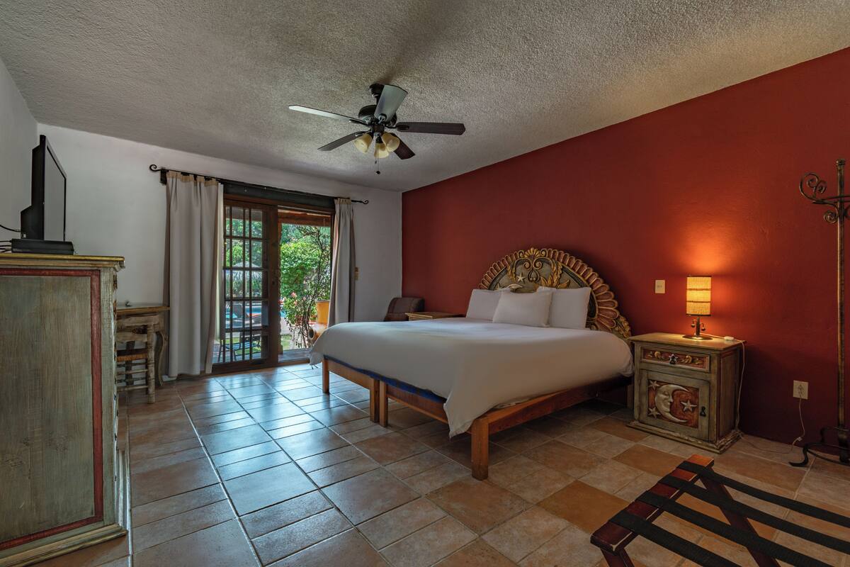 A bedroom with a bed, a ceiling fan, a nightstand, and a view of the outdoors through a sliding door.