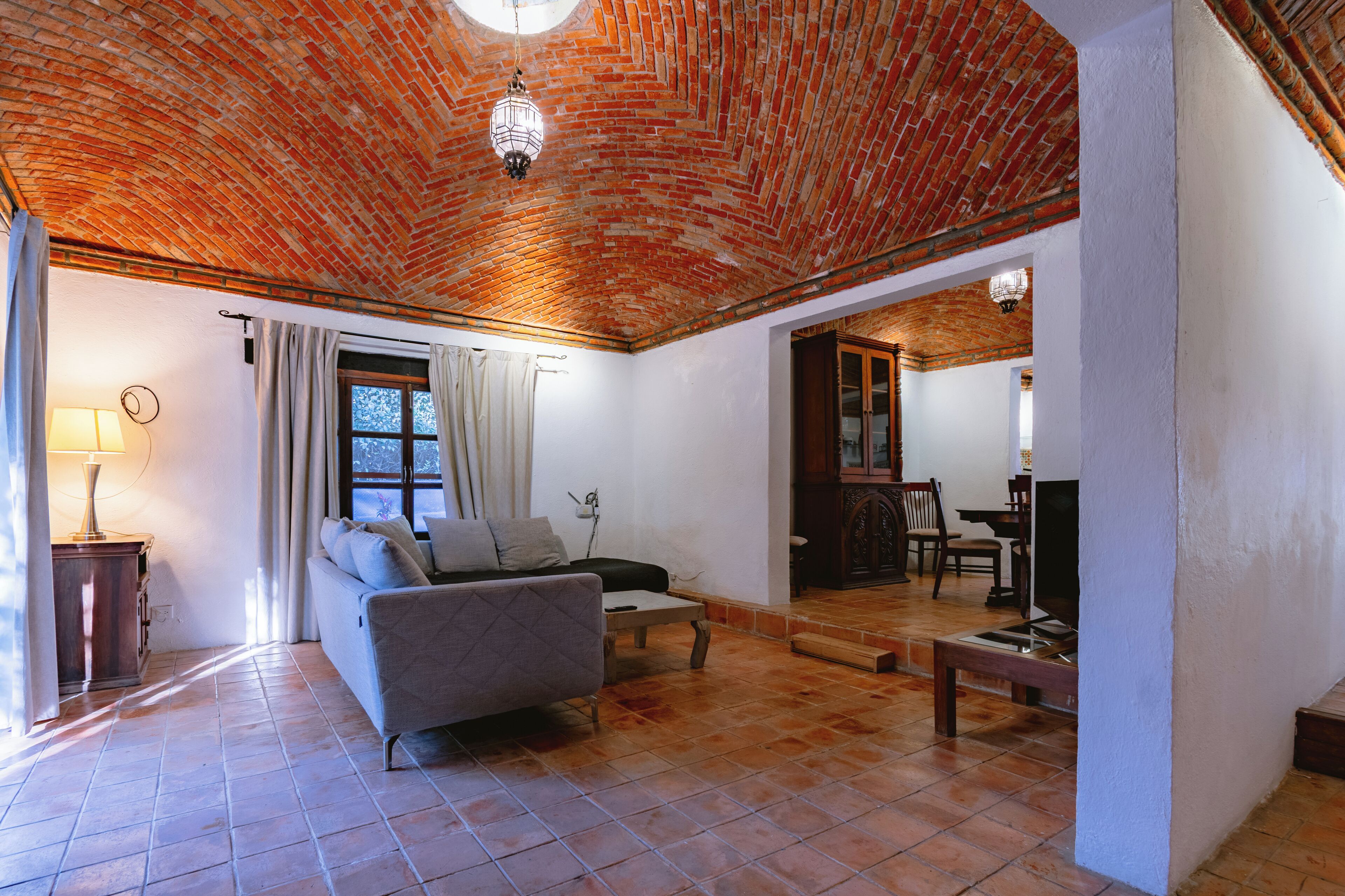 Una sala de estar con techo de ladrillo, un sofá, un televisor y una zona de comedor.