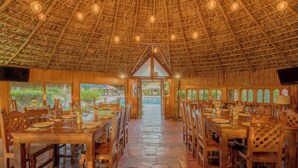 A restaurant with a thatched roof, wooden tables and chairs, and large windows offering views of greenery. - Hotel Atotonilco El Viejo (San Miguel de Allende)