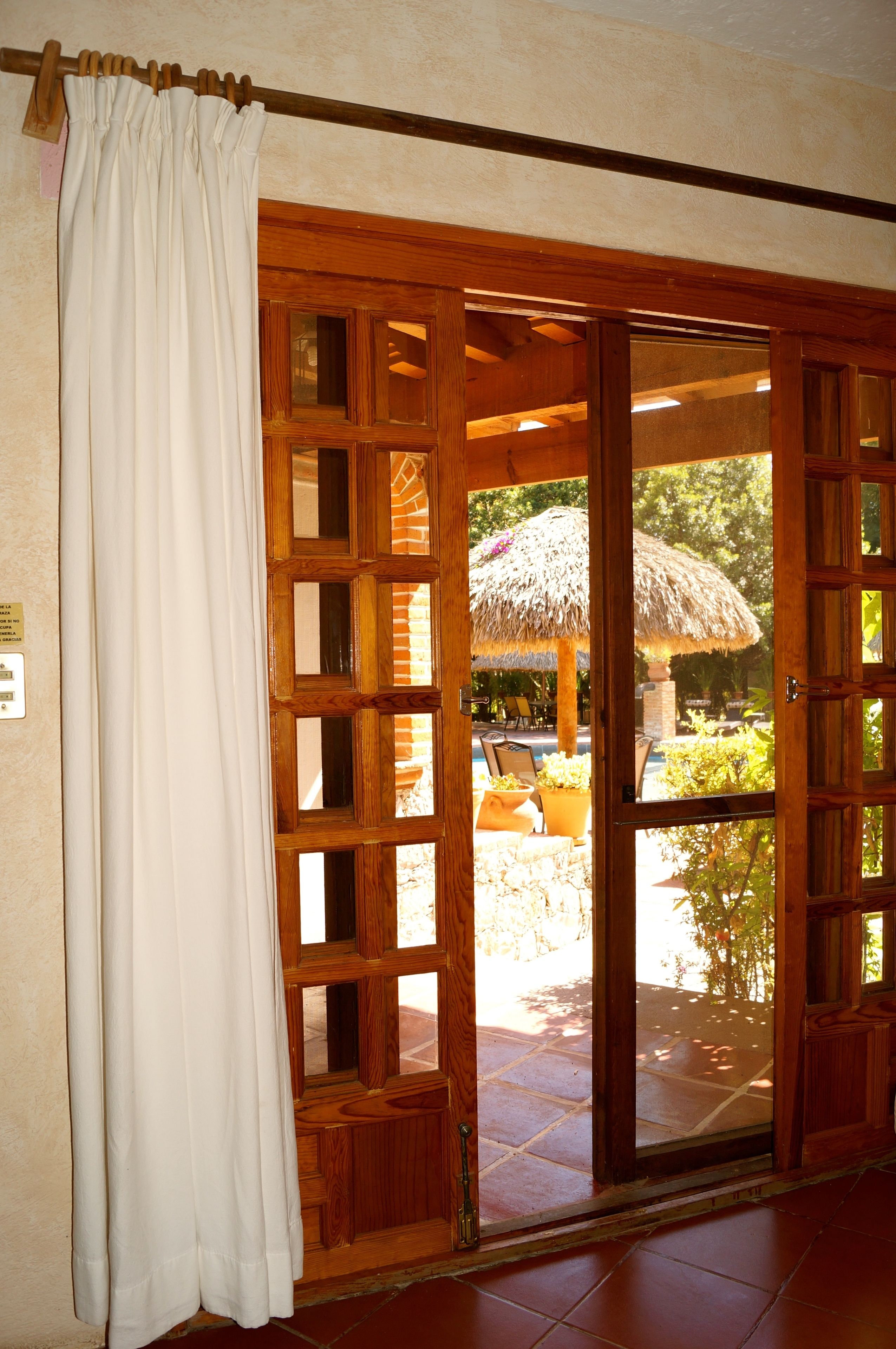 A wooden sliding door with glass panels, leading to an outdoor patio with a thatched umbrella and potted plants.