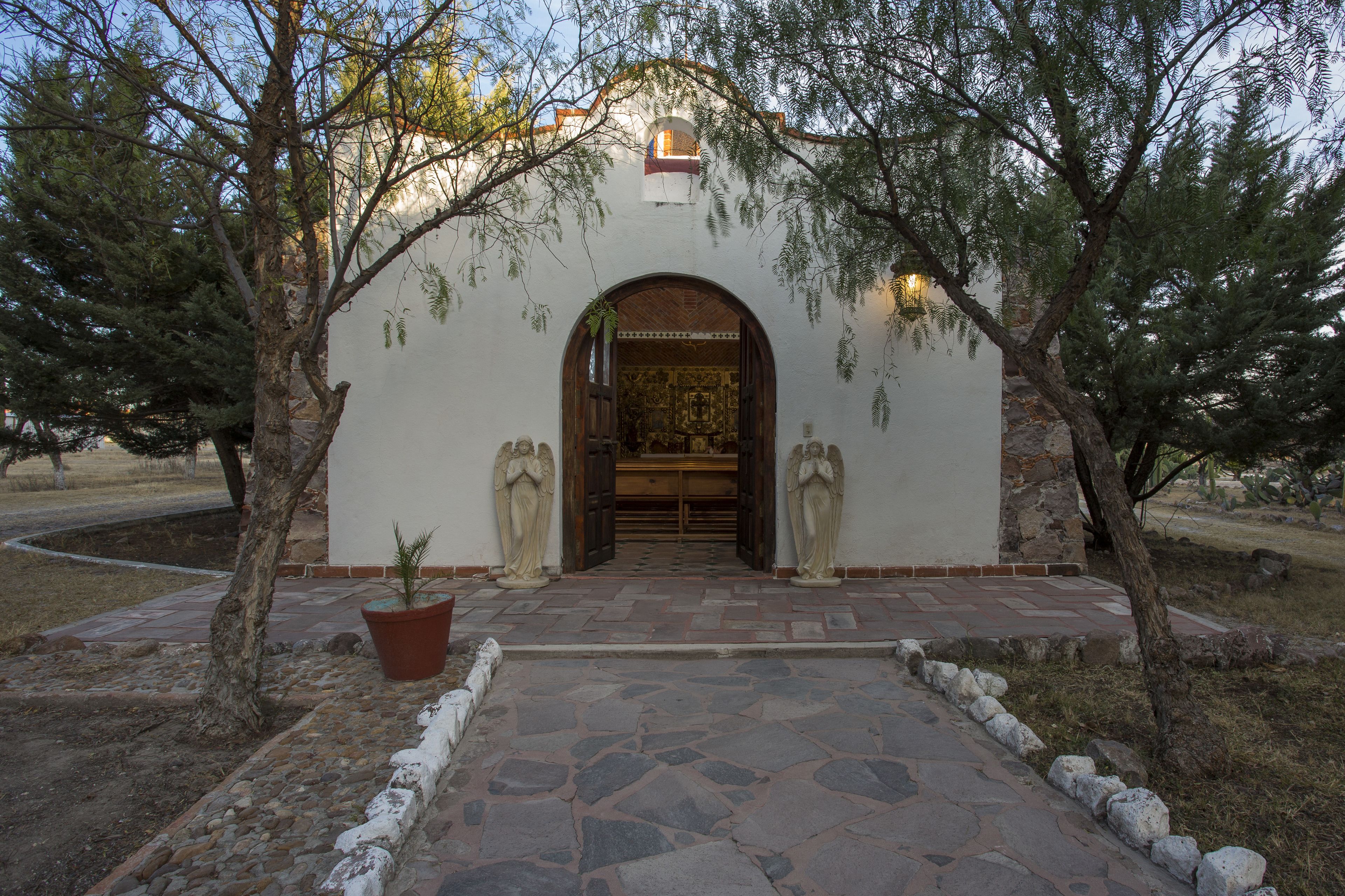 A building entrance with a stone pathway leading to an arched doorway, flanked by two statues and a potted plant.