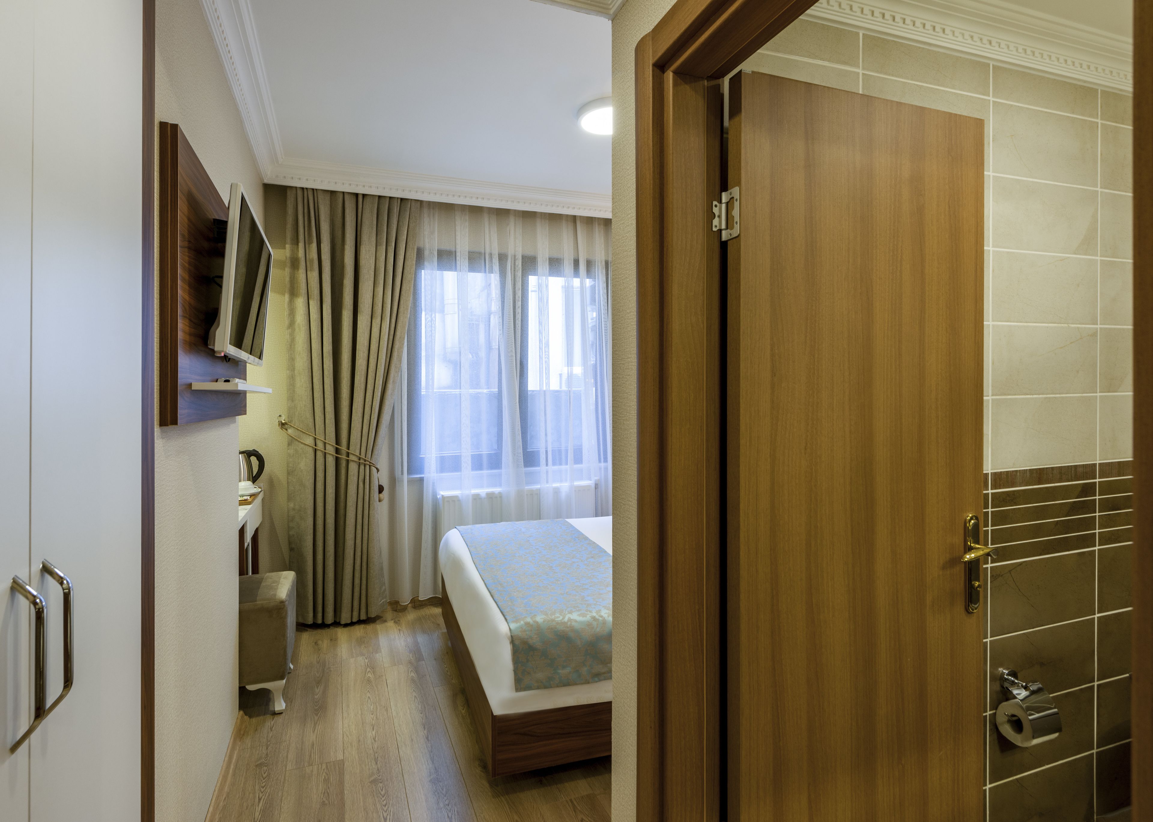 Une chambre d’hôtel avec un lit, des rideaux, un téléviseur fixé au mur et une porte en bois.