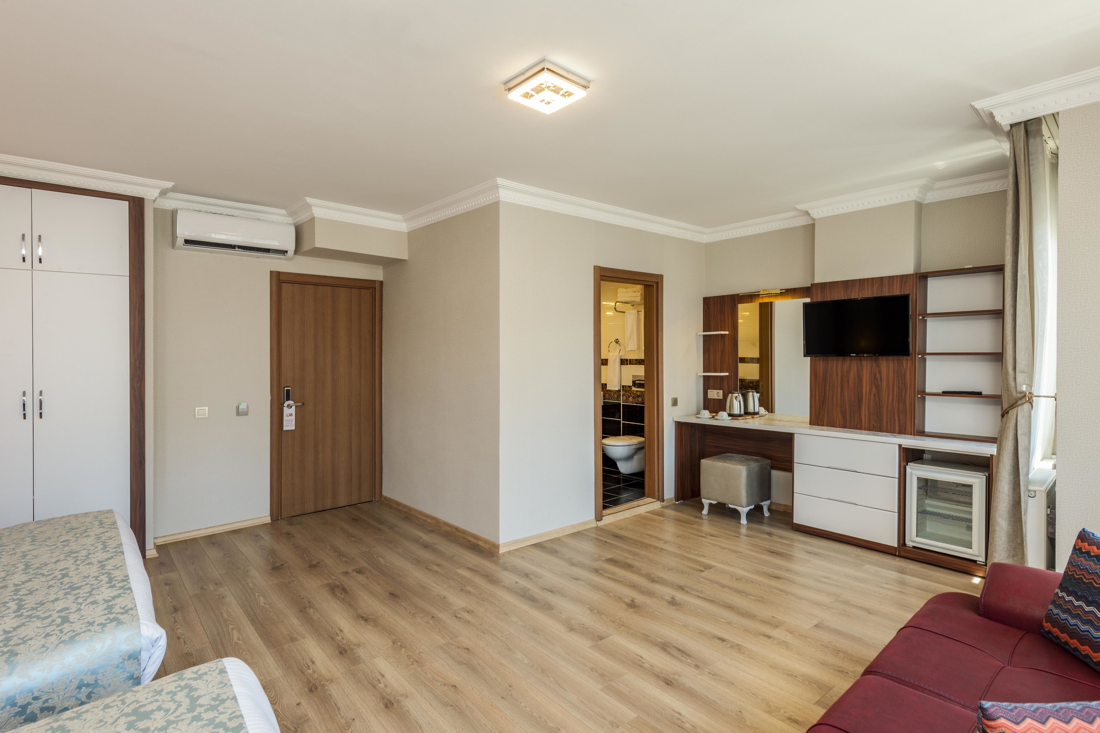 Eine moderne Wohnung mit Holzboden, einem Wohnbereich inklusive Sofa und Fernseher, einer Küchenzeile und einem durch eine offene Tür einsehbaren Badezimmer.