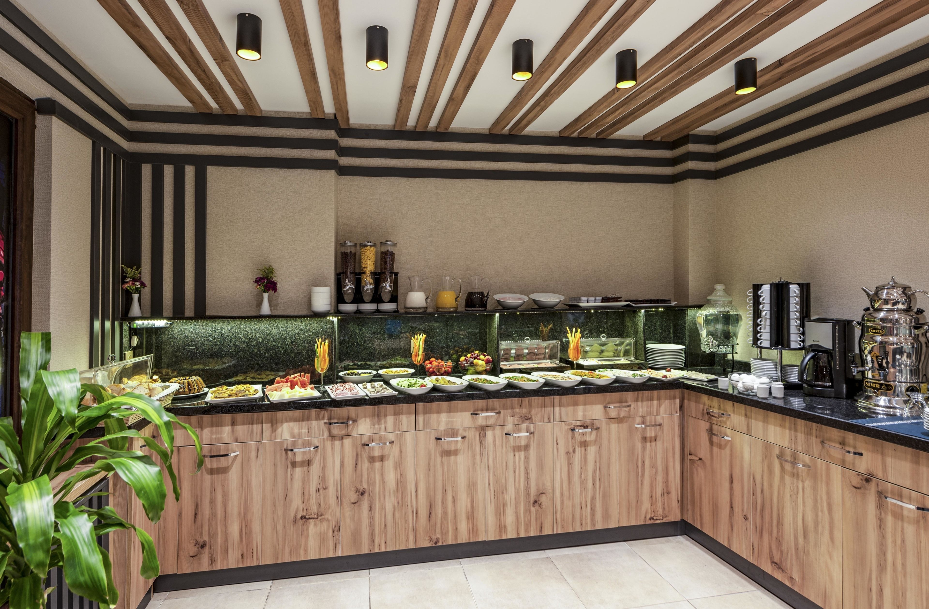 Un'area buffet con diversi cibi e bevande, mobili contenitori in legno e un moderno design del soffitto.