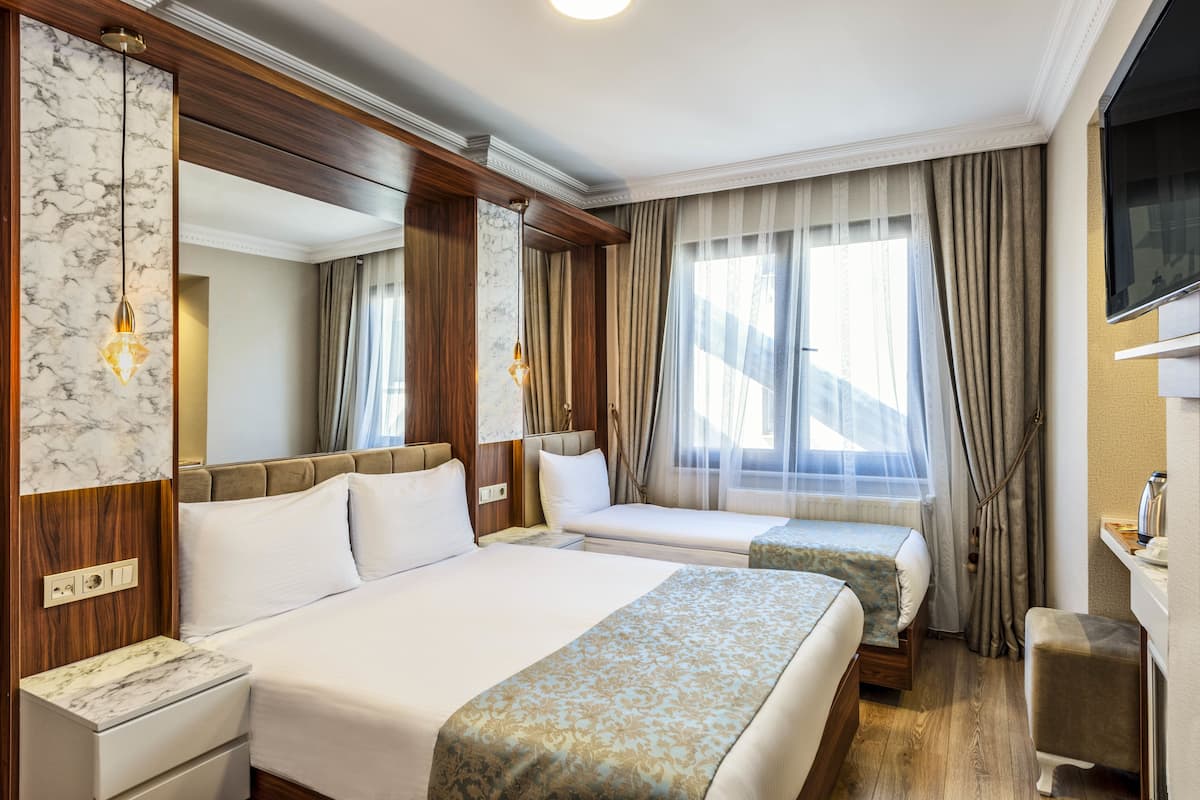 Une chambre d’hôtel avec deux lits, une tête de lit en bois, un mur décoratif en marbre, une télévision et un petit bureau avec une chaise.