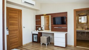 A bedroom with a wooden wardrobe, a small bedside table, a TV mounted on the wall, and a built-in sink. - Hotel Kupeli (Istanbul)