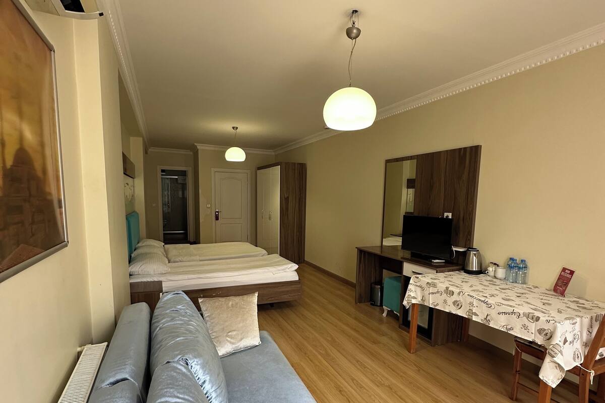 Une chambre d’hôtel avec un canapé, une table à manger recouverte d’une nappe, un téléviseur et un miroir.