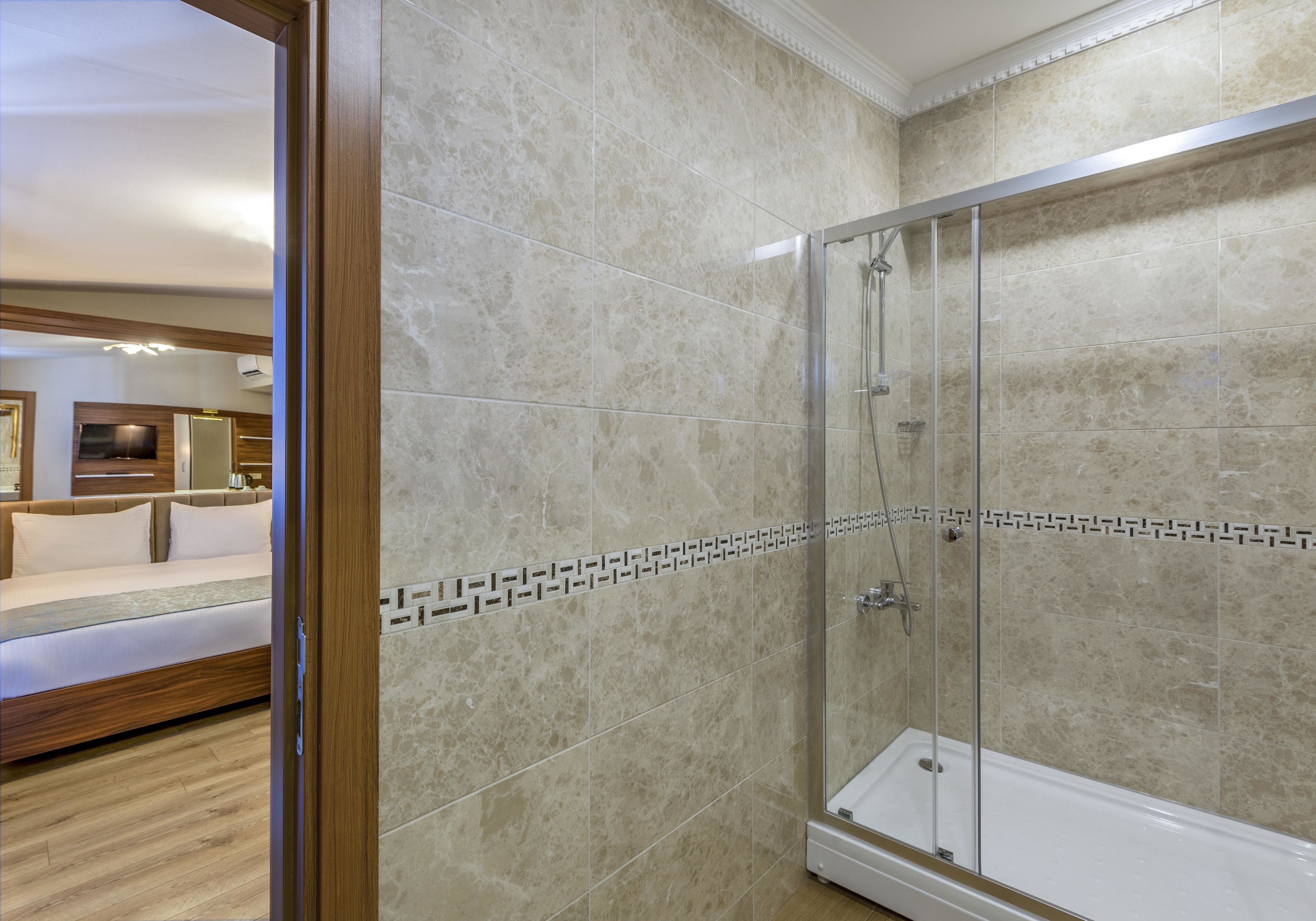 A modern bathroom with a glass-enclosed shower, beige marble tiles, and a patterned border.