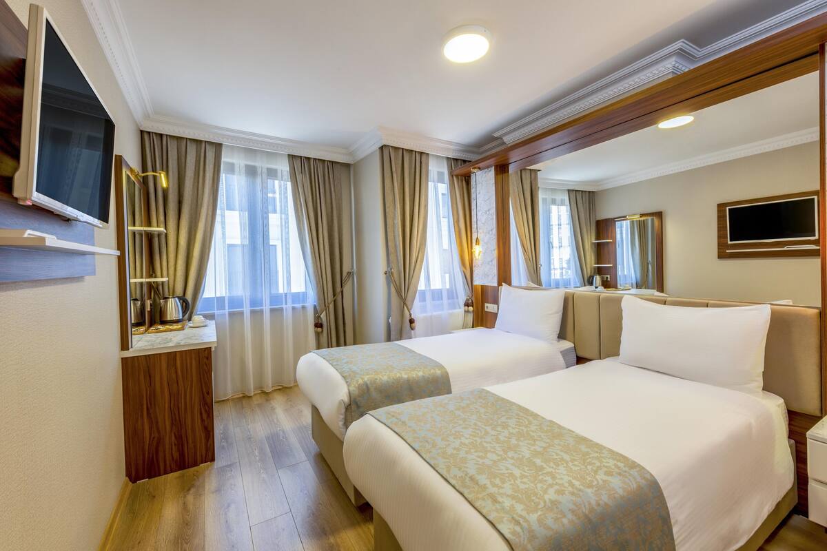 Une chambre d’hôtel avec deux lits, une télévision, un bureau avec une lampe et une grande fenêtre avec des rideaux.