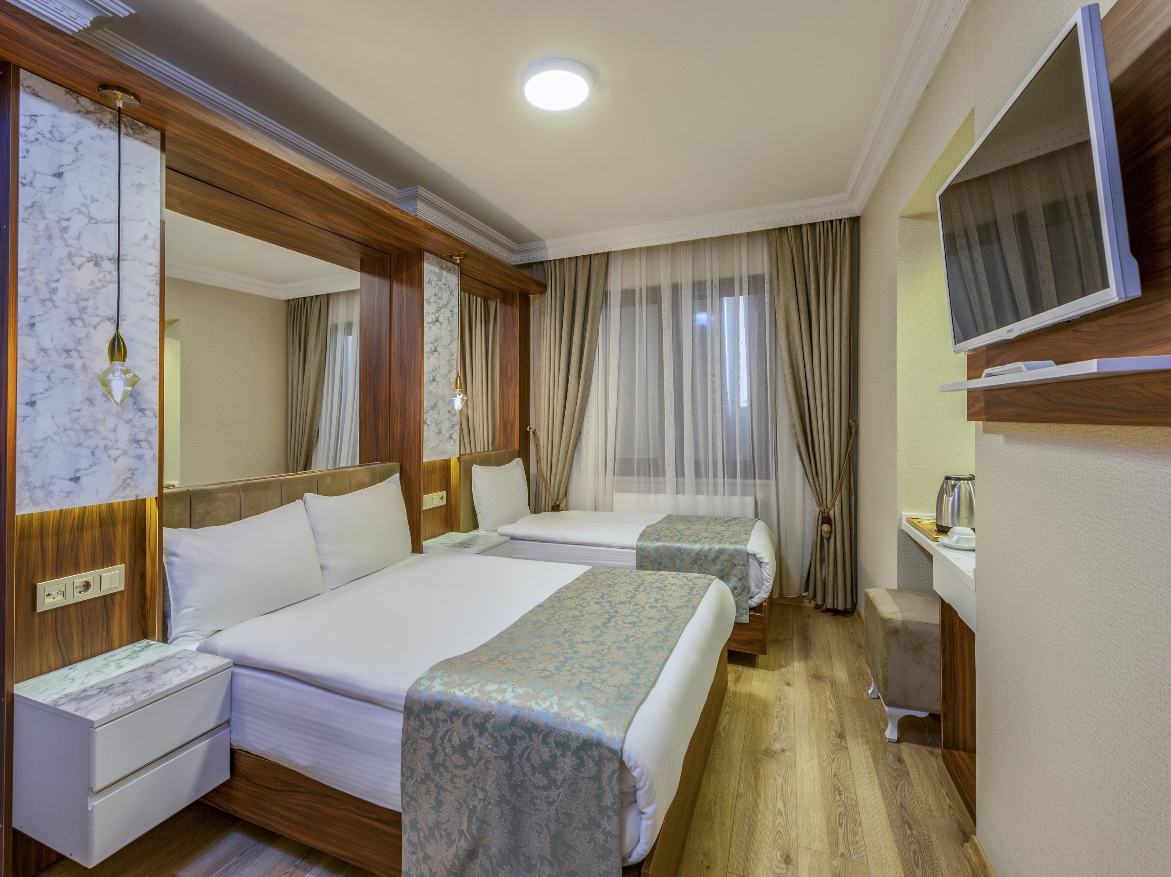 Una camera d'albergo con due letti, una TV, un comodino con lampada e un angolo cottura.
