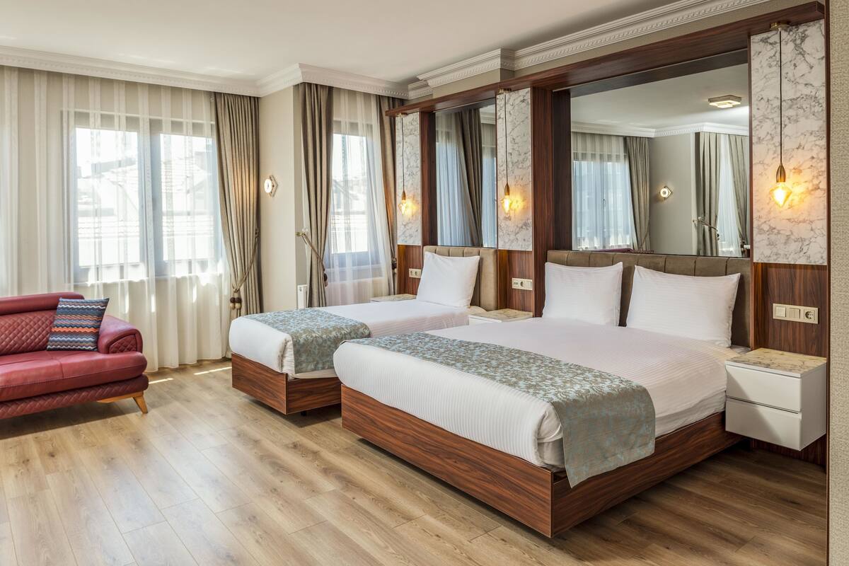 Une chambre d’hôtel avec deux lits, un canapé rouge, un plancher en bois et un grand miroir.