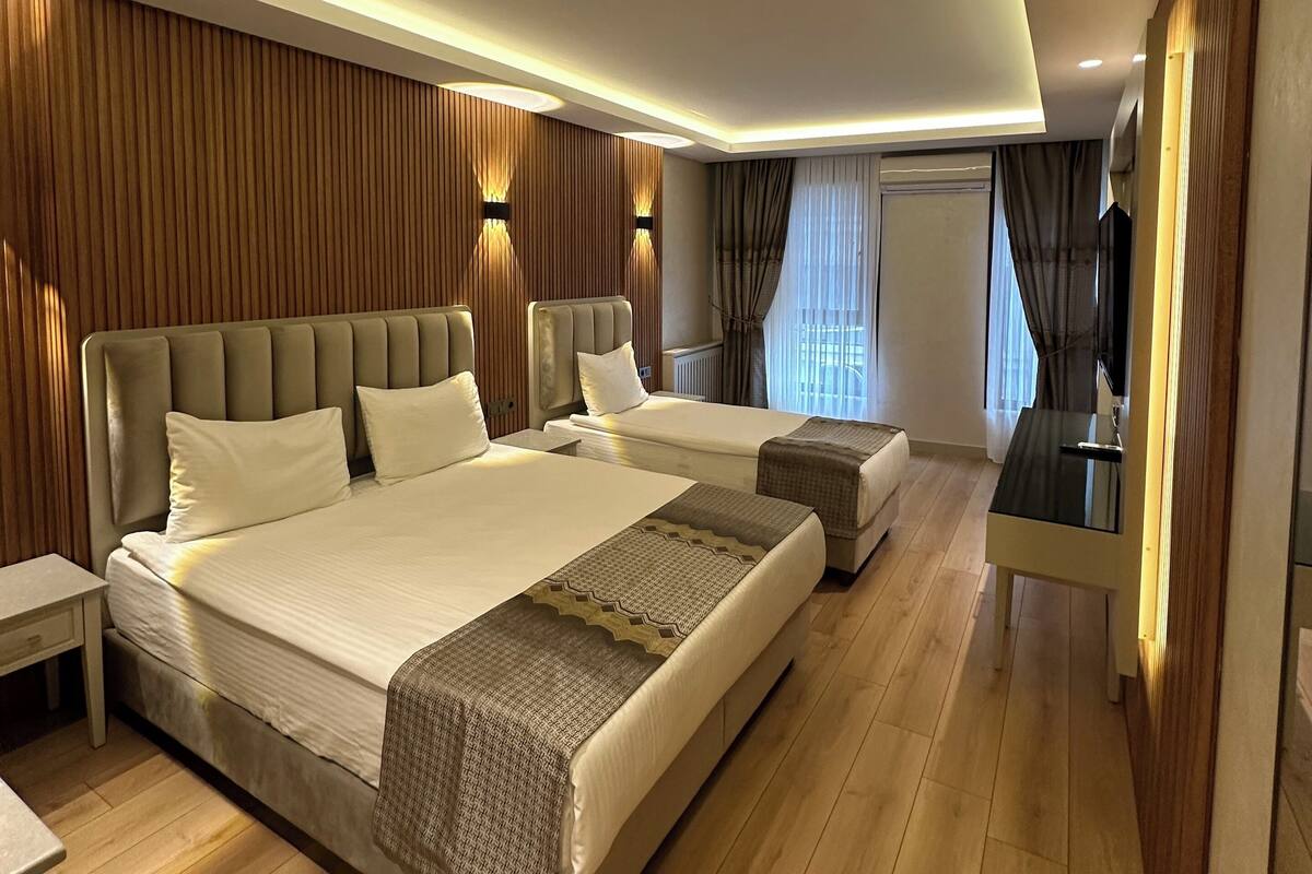 Une chambre moderne avec deux lits, une table de chevet, un téléviseur et un mur d’accent en bois.