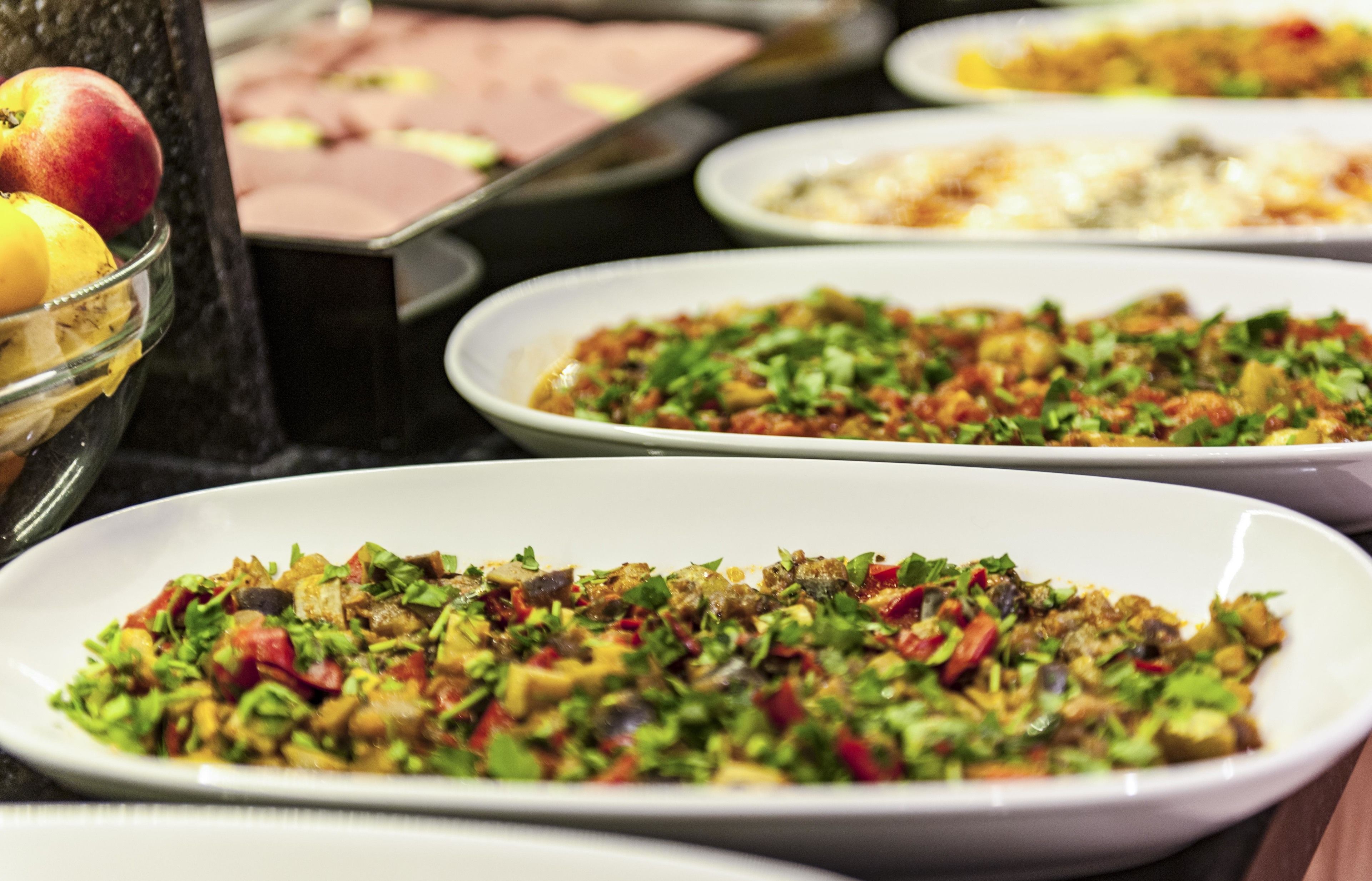 A buffet with various dishes, including a salad with chopped vegetables and a bowl of fruit.