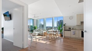 A modern apartment with a living room, dining area, and kitchen. It features large windows, a flat-screen TV, and a city view.