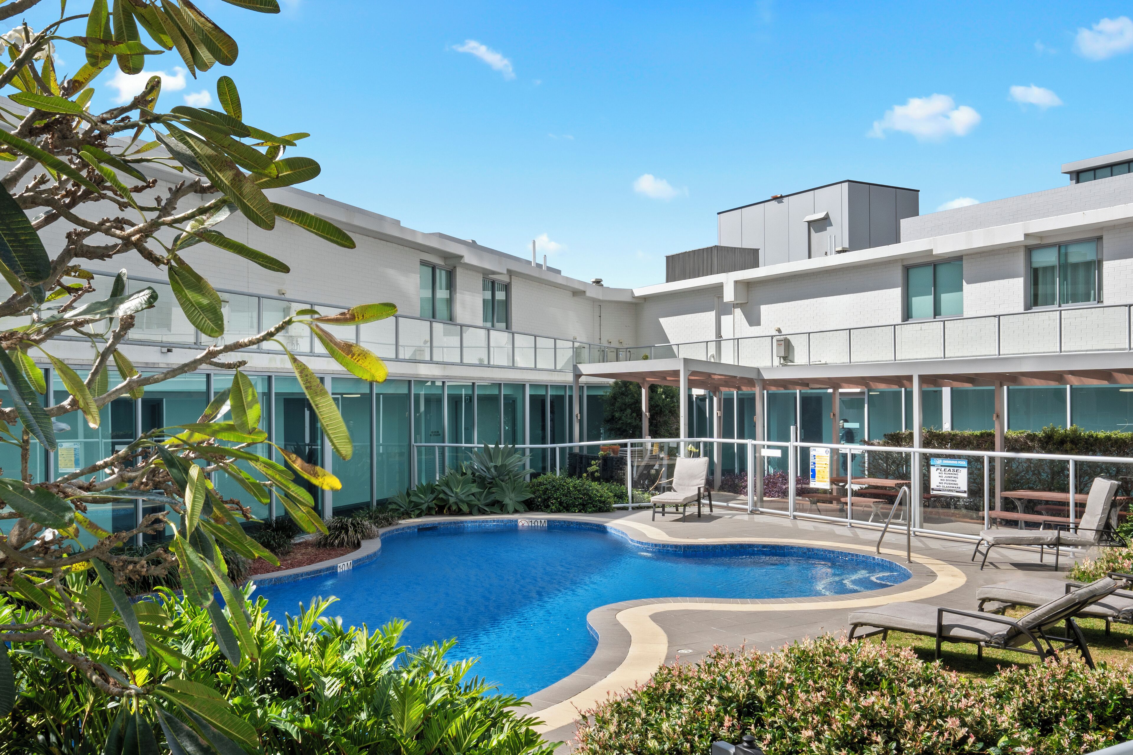A modern building with a swimming pool surrounded by lounge chairs and greenery.