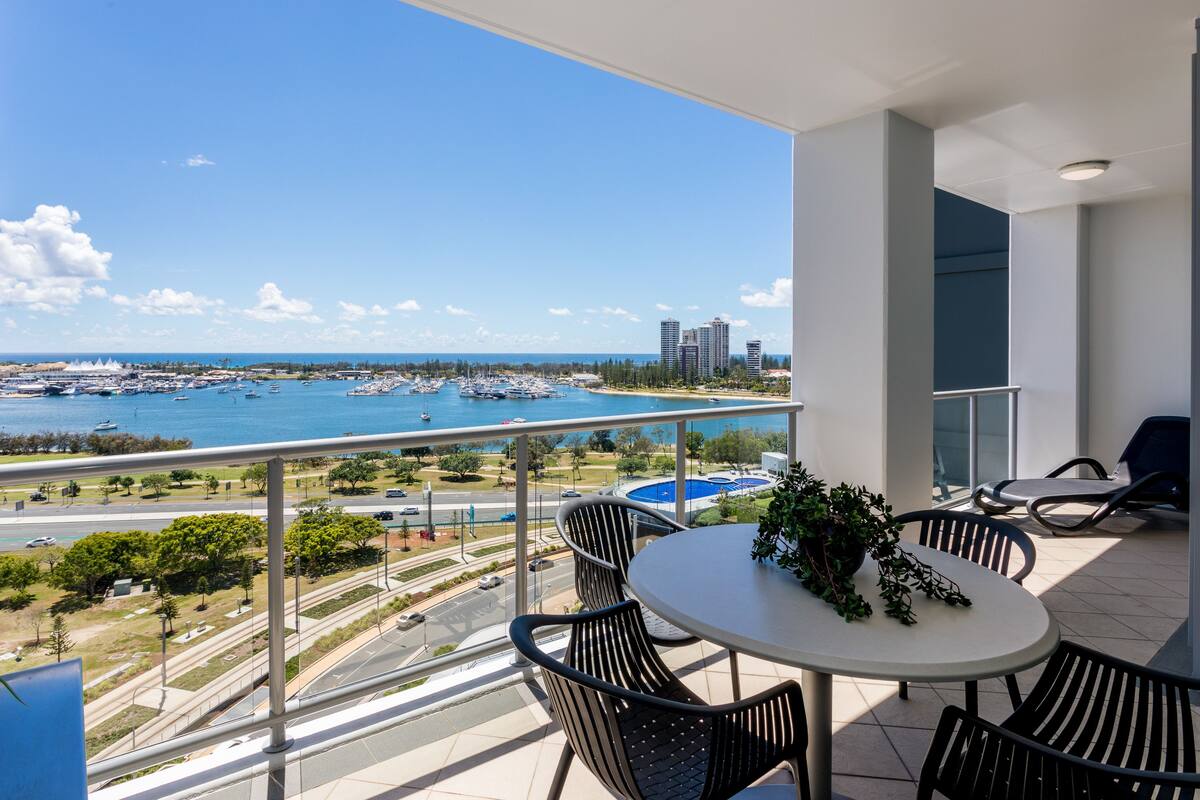 A balcony with a table and chairs, overlooking a marina with boats and buildings.