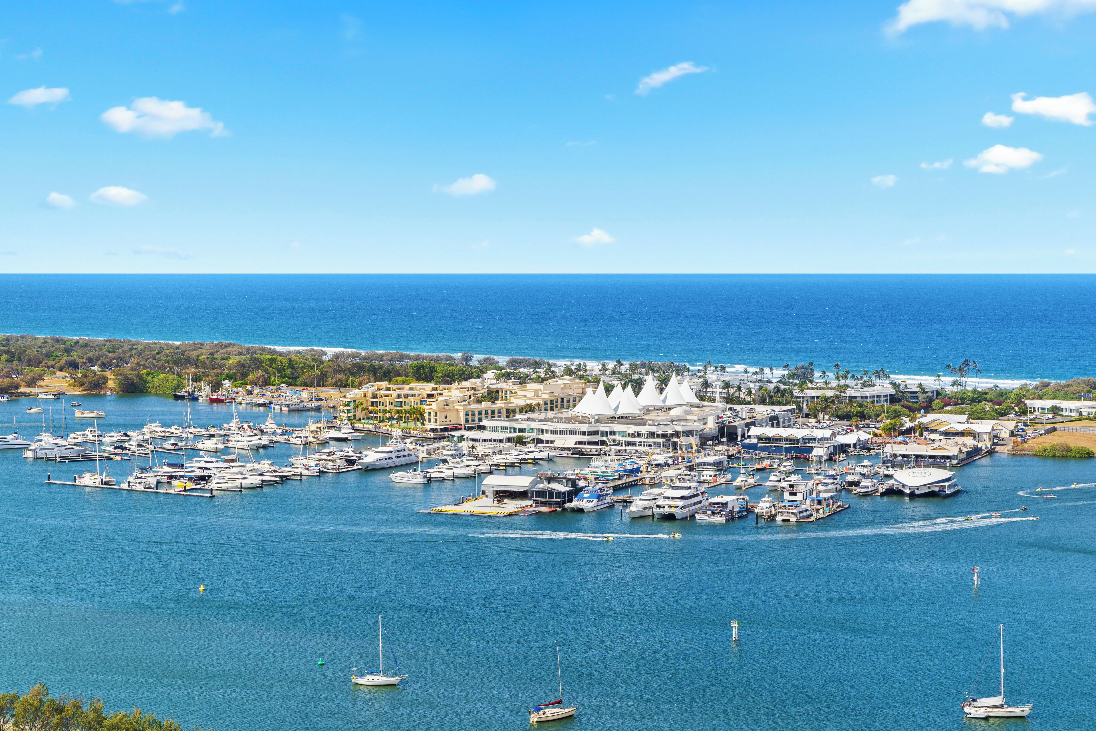 Un port de plaisance où de nombreux bateaux sont amarrés, entouré de bâtiments et surplombé par un ciel bleu clair.