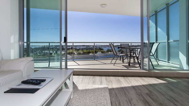 A modern living room with a white sofa, a glass table, and a view of a cityscape through large windows.
