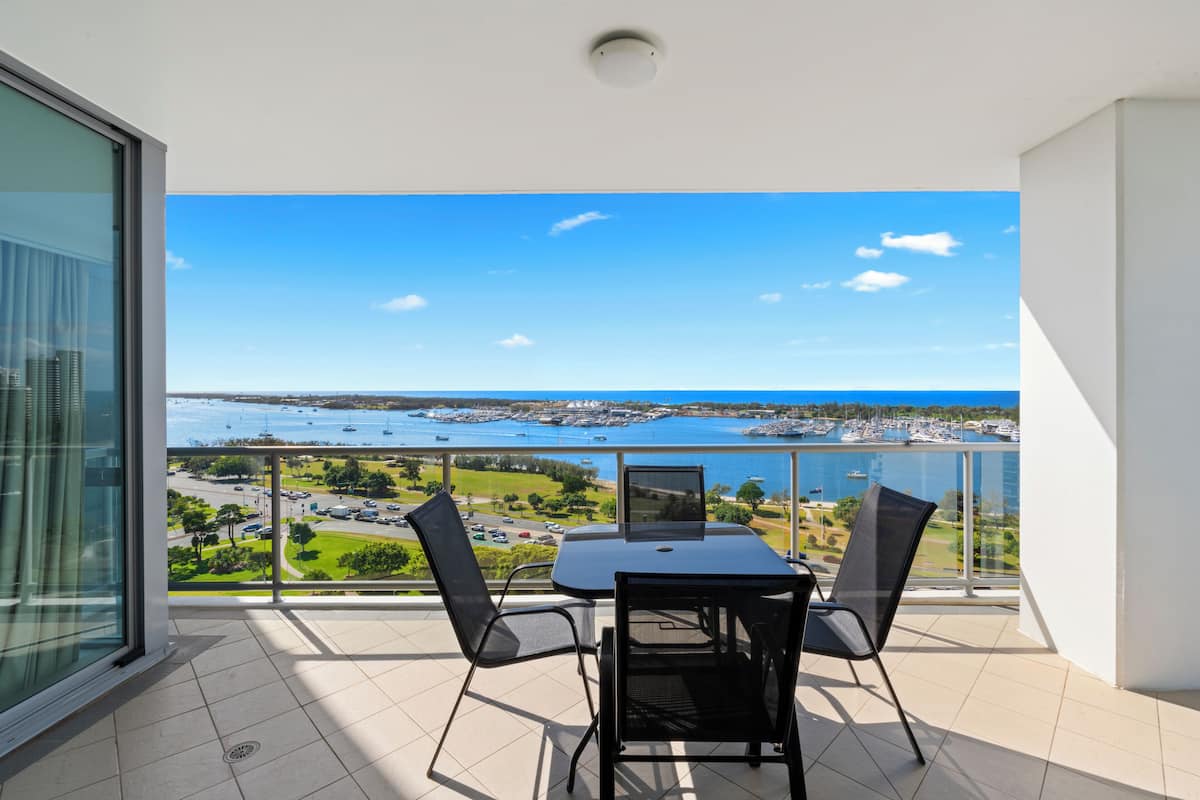 A balcony with a table and chairs, overlooking a marina with boats and a distant cityscape.
