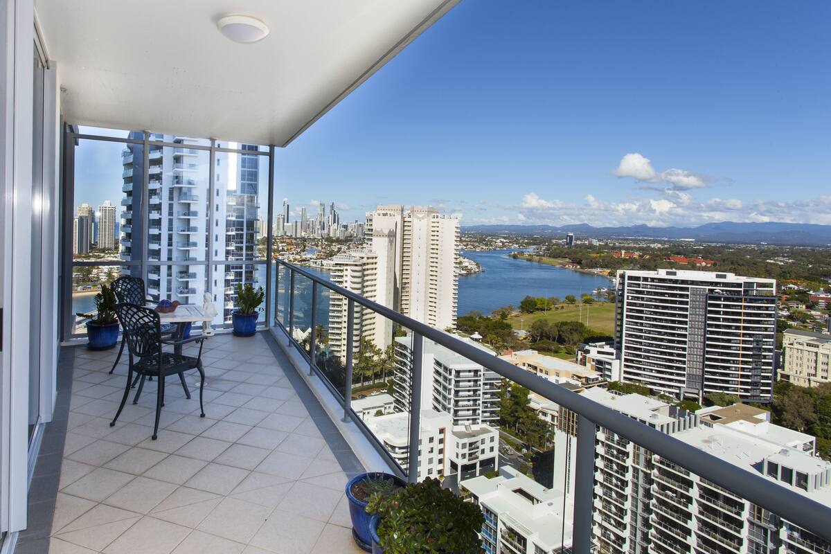 A balcony with a table and chairs, overlooking a cityscape with high-rise buildings and a body of water.