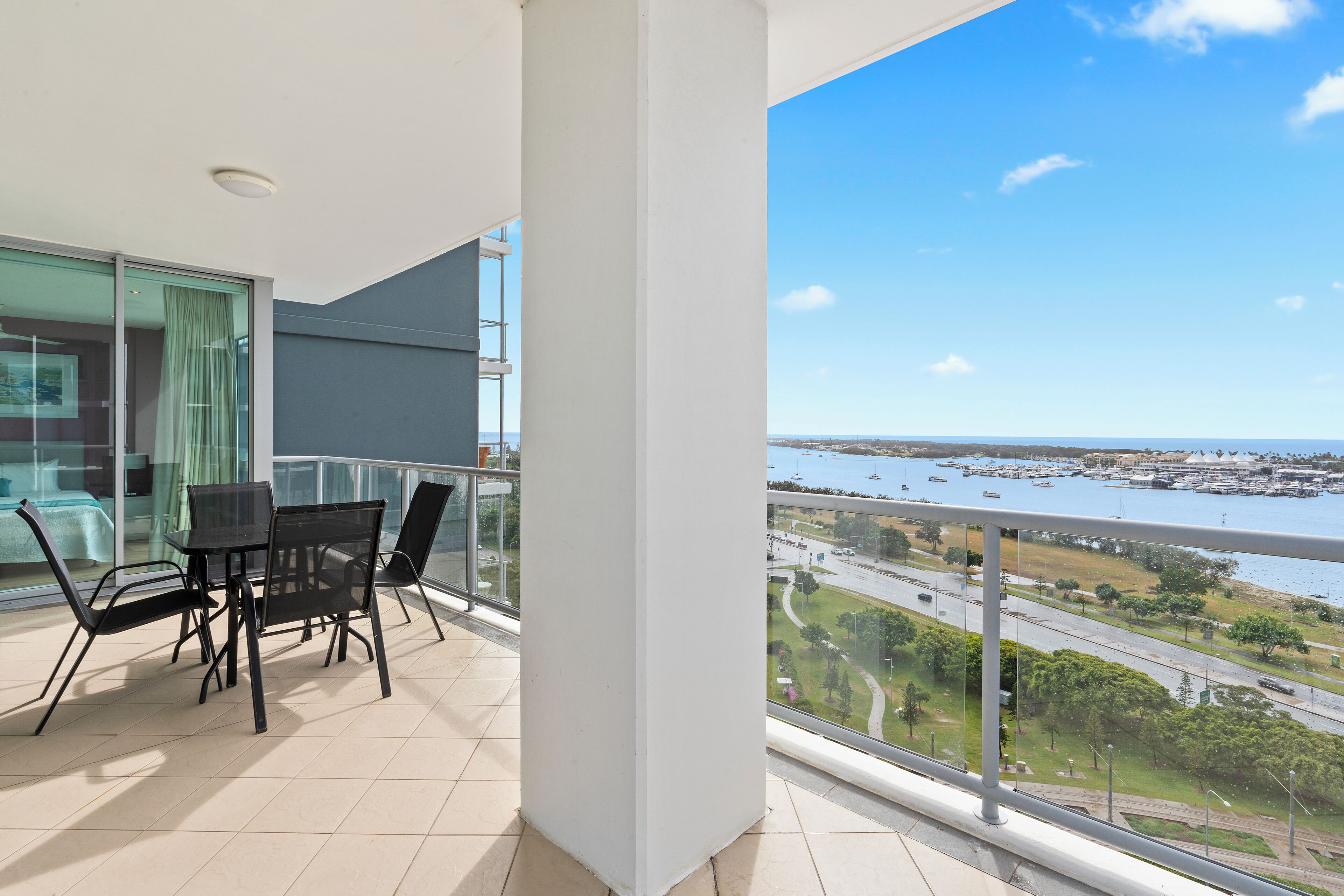 A balcony with a table and chairs, a glass door, and a view of a marina and roads.