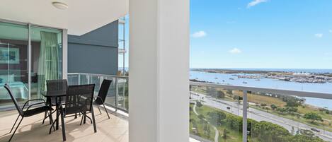 A balcony with a table and chairs, a glass door, and a view of a marina and roads.