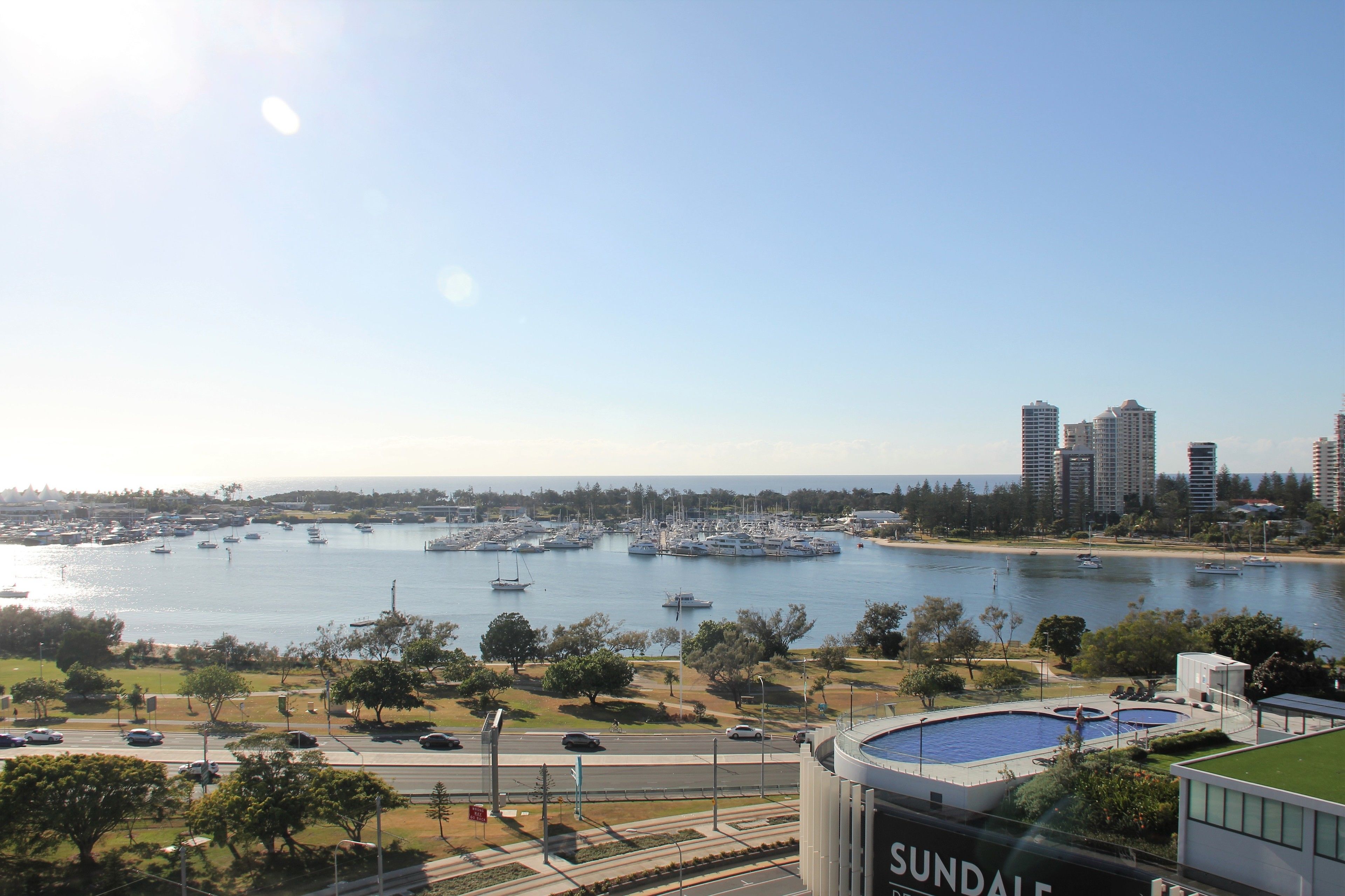 A marina with boats, a city skyline, and a road with cars.