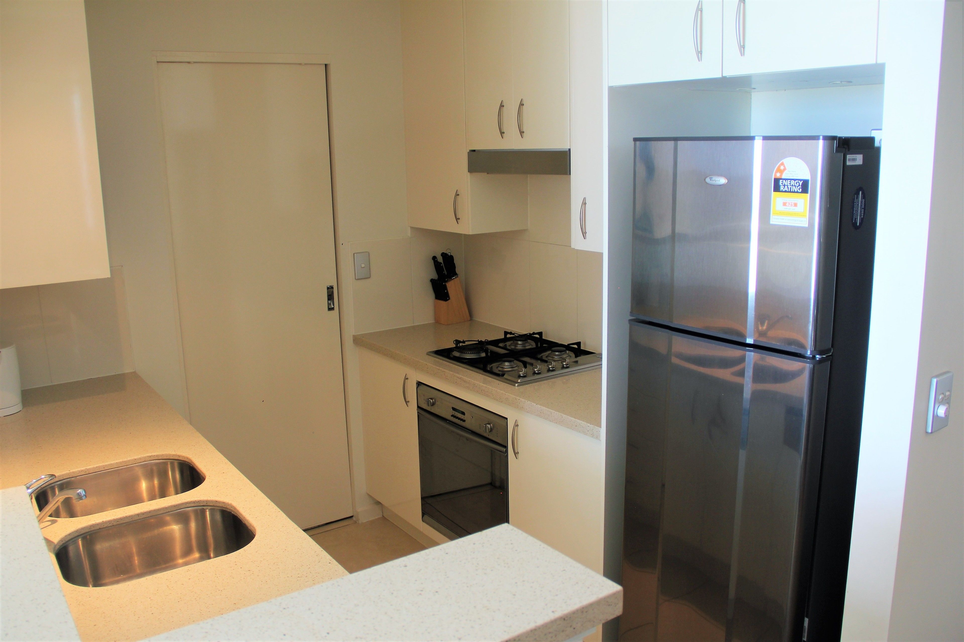 Cocina compacta con refrigerador de acero inoxidable, pileta doble, estufa y muebles de cocina blancos.
