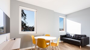 A modern living room with a round table, four chairs, a sofa, and large windows with city views. - Mayfair Plaza Motel (Sandy Bay)