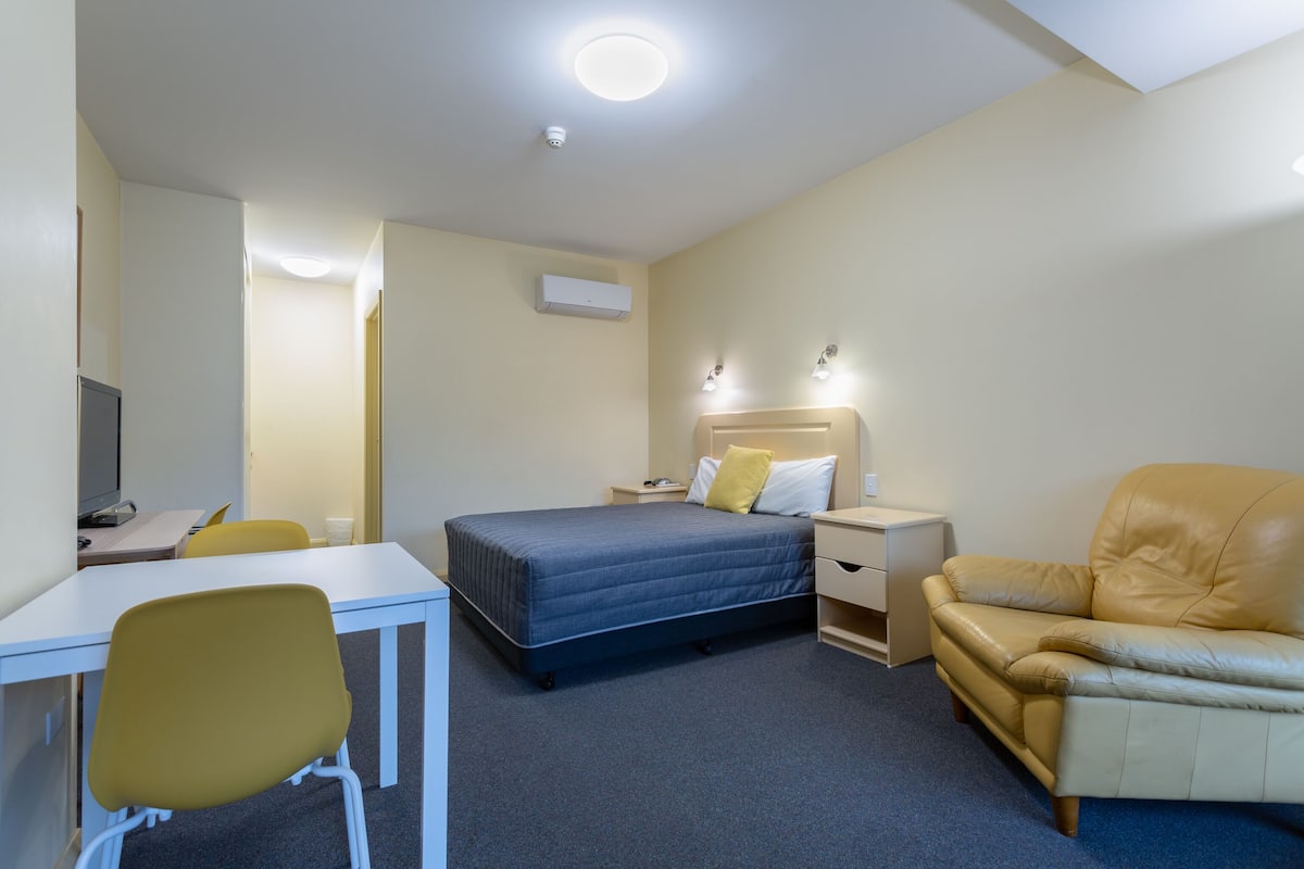 Hotellihuone, jossa on sänky, työpöytä, tuoli, sohva ja televisio.