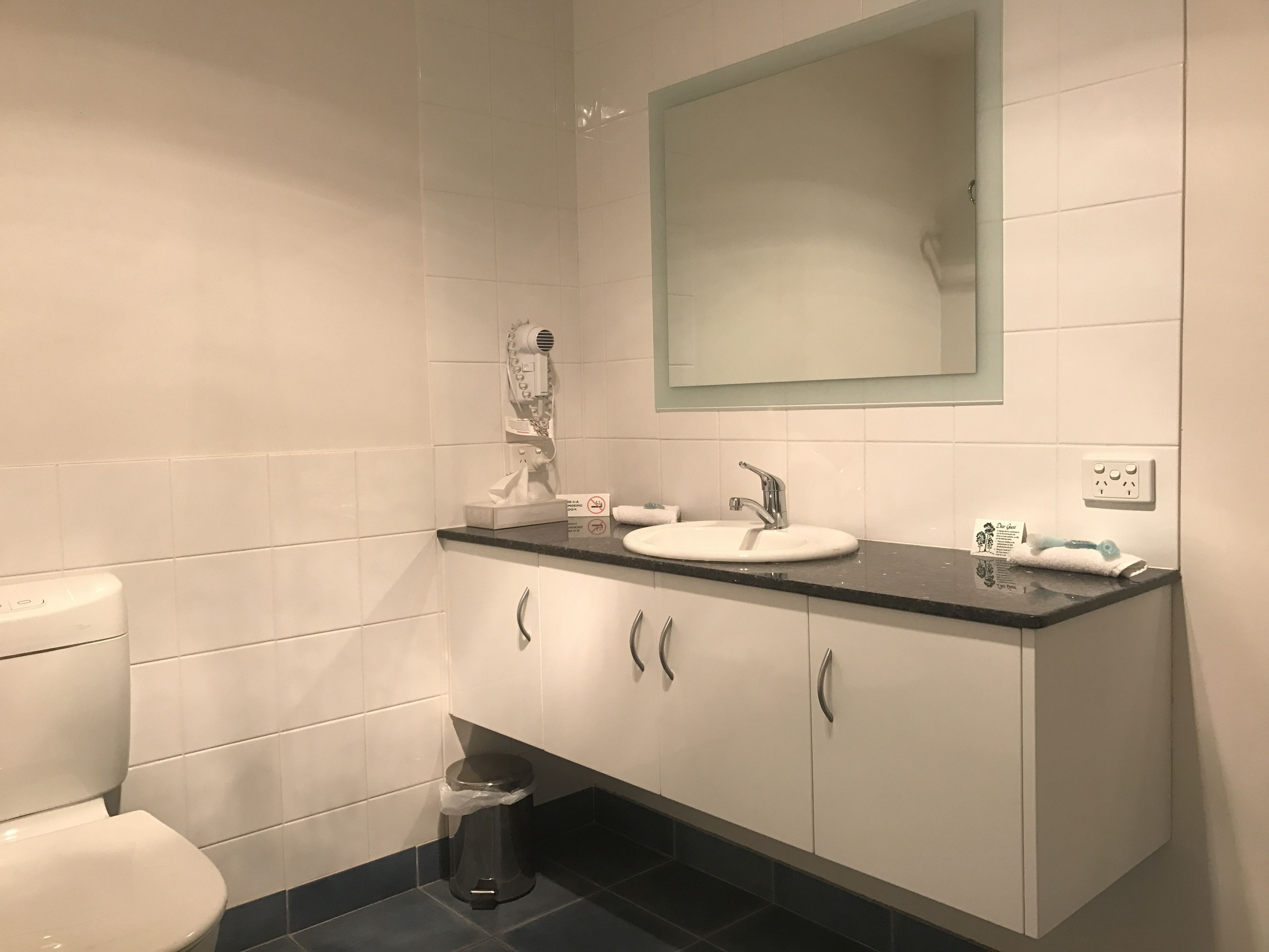 Un baño con un inodoro blanco, un lavamanos con un espejo encima y un cubo de basura.