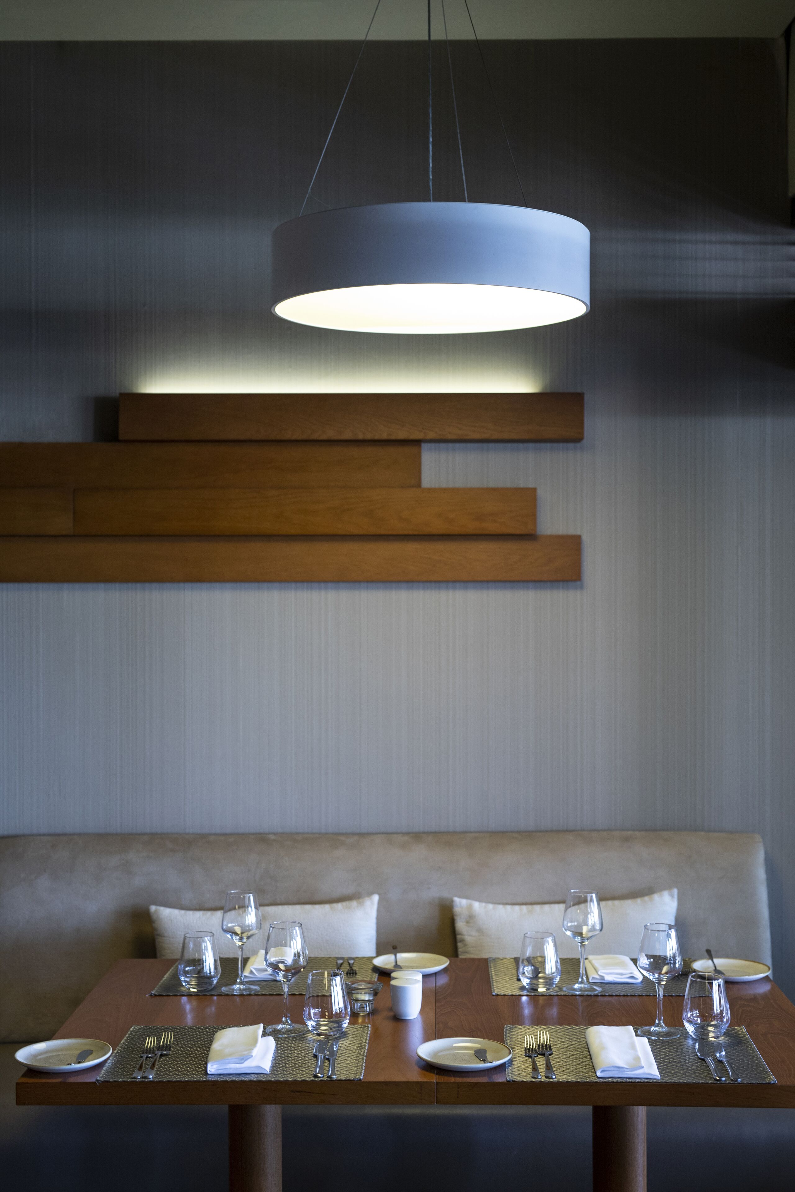 A dining area with a wooden table set for two, a bench, and a hanging light fixture.