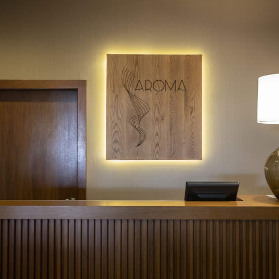 A reception desk with a wooden panel displaying the word "AROMA" and a lamp on the right.