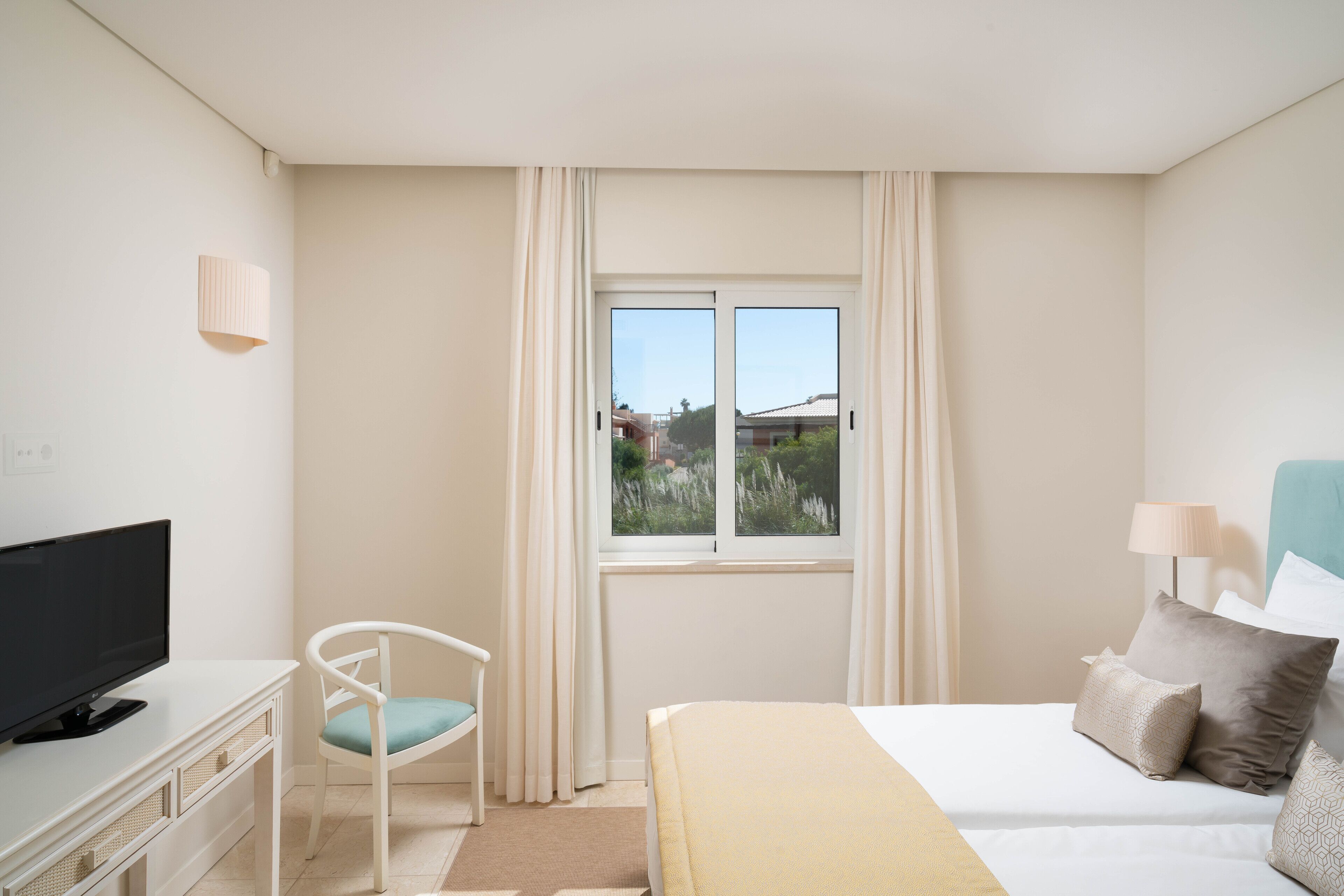 A hotel room with a bed, a TV, a chair, and a window with curtains.