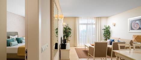 A hotel room with a bed, a dining area with chairs and a table, a large mirror, and a potted plant.