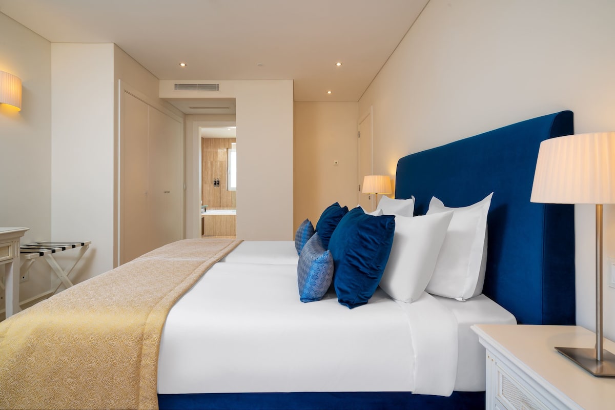 A modern hotel room with a large bed, a bedside table, and a lamp.