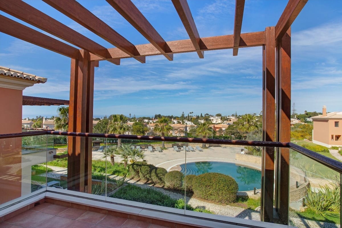 A balcony with a view of a swimming pool, palm trees, and a residential area.